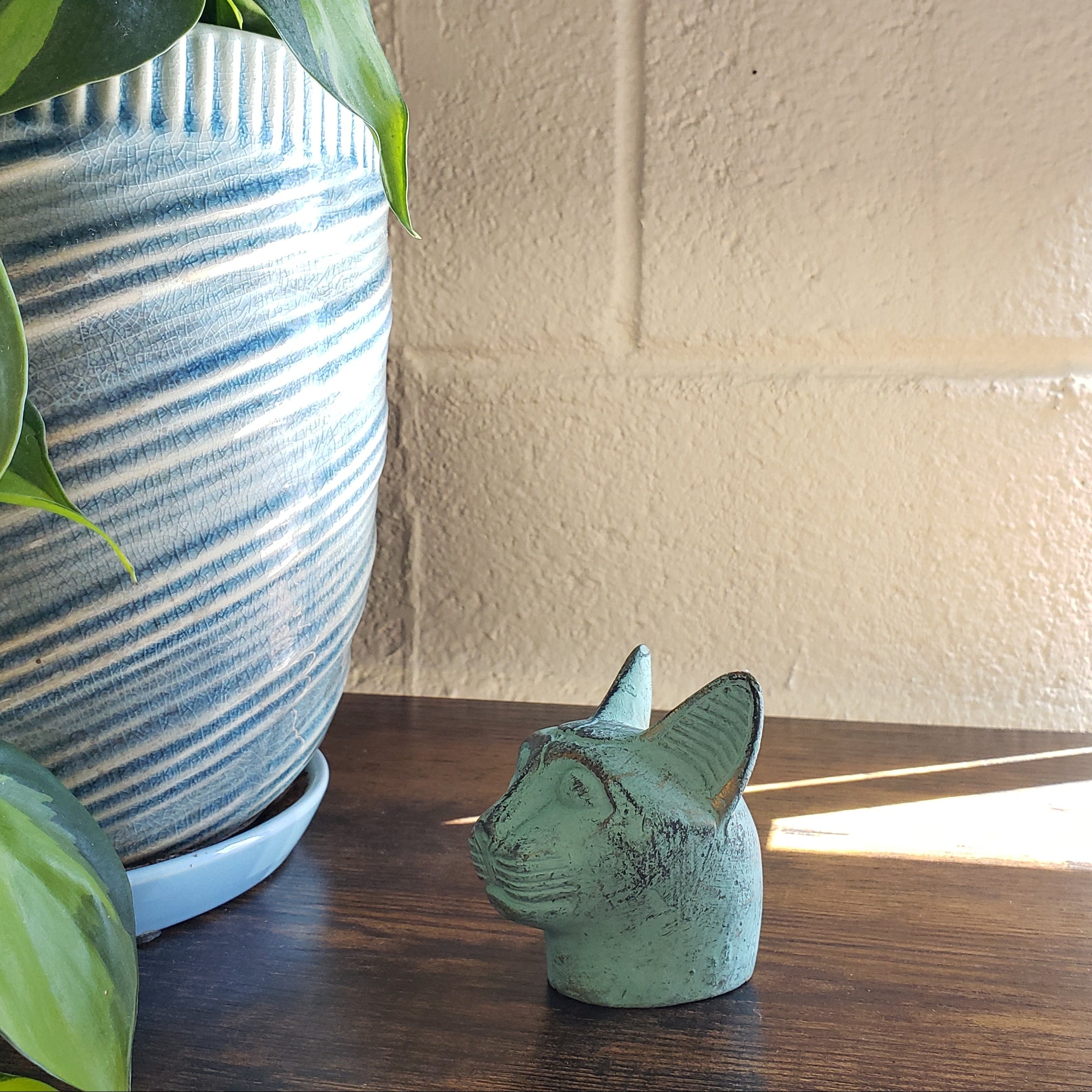 Green cat-shaped object on a textured wall with plants in the foreground