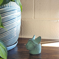 Green cat-shaped object on a textured wall with plants in the foreground