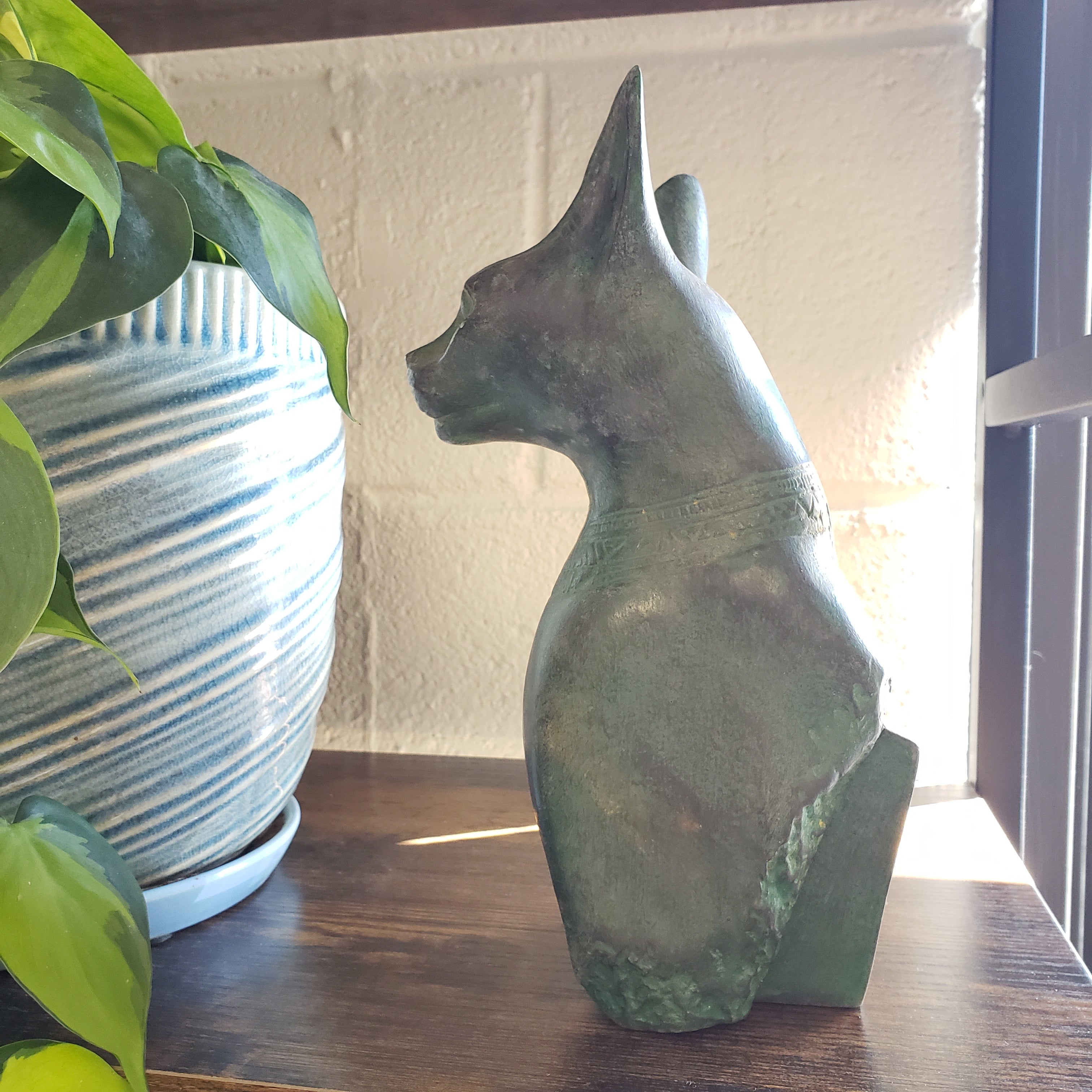 Decorative Patina statue of a cat on a wooden board with plants in the foreground.