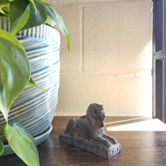 Small statue on a shelf with plants and a light fixture in the background