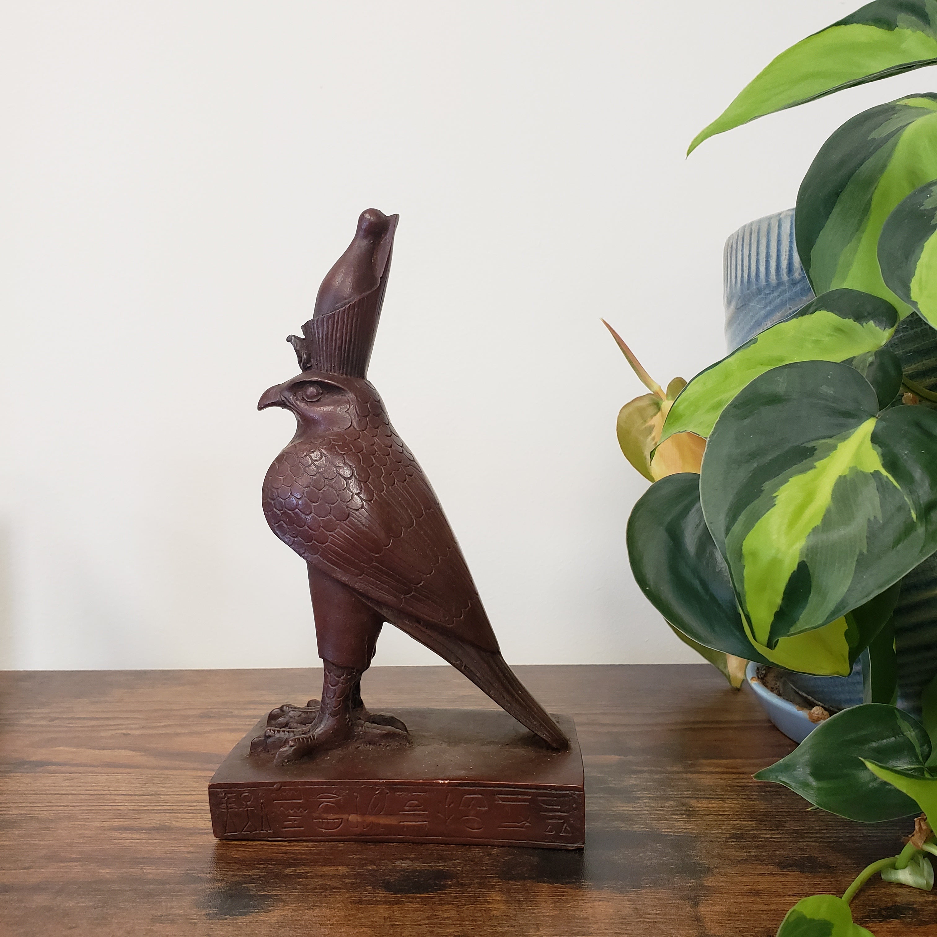 Egyptian falcon-god Horus sculpture on a wooden block with green plants in the background