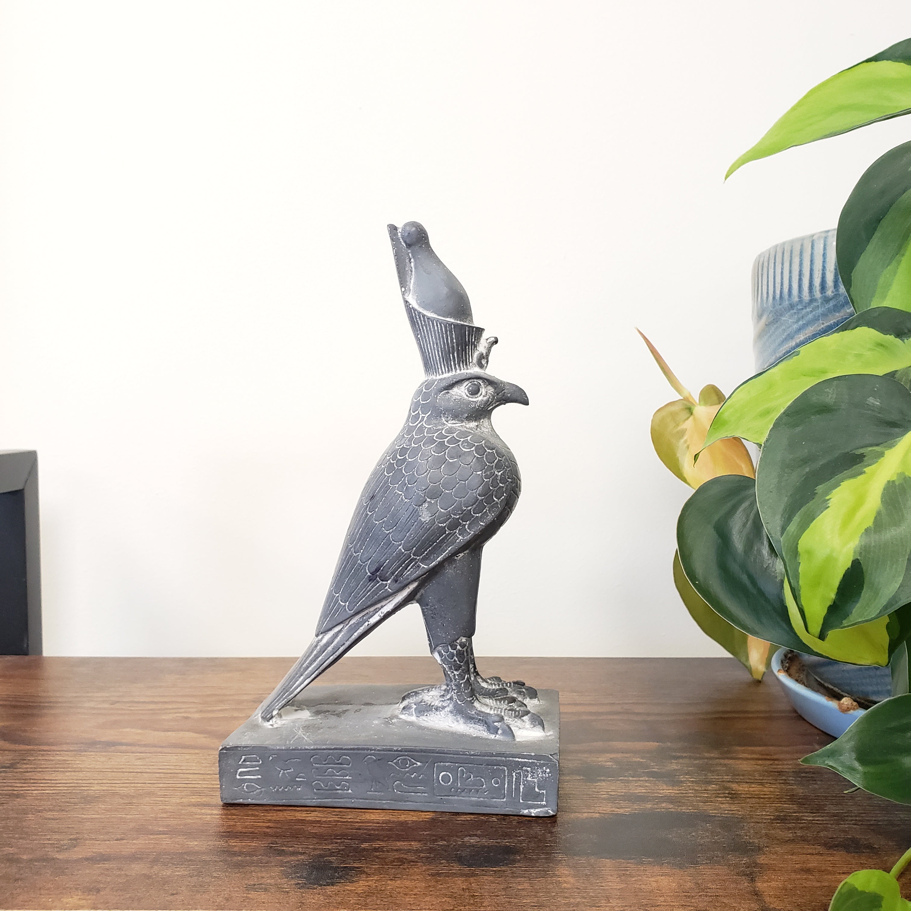 Decorative Egyptian falcon-god Horus sculpture on a wooden surface with plants in the background