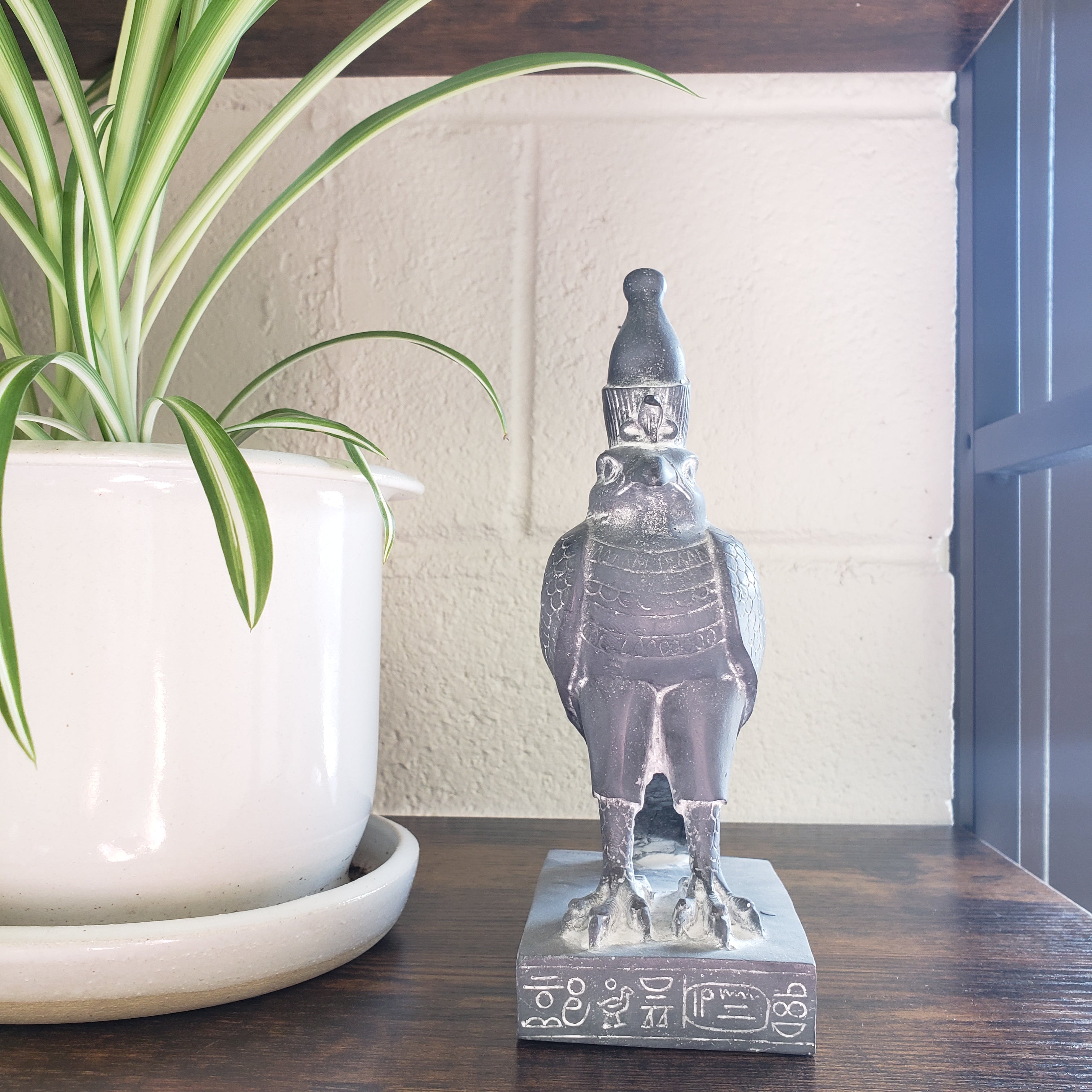 Decorative Egyptian falcon-god Horus statue and plant in a wooden cabinet.