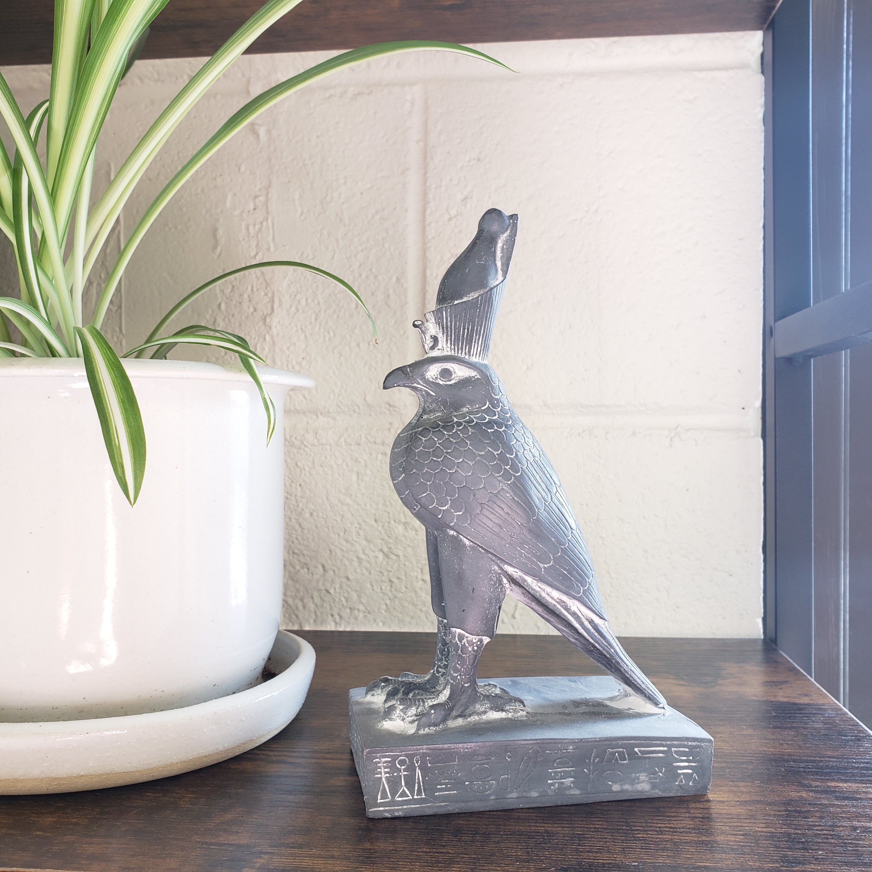 Decorative Egyptian falcon-god Horus sculpture on a shelf with a plant in the foreground