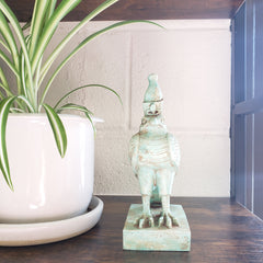 Decorative green Egyptian falcon-god Horus statue on a white pedestal with a plant in the foreground.