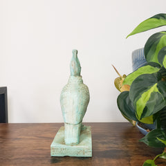 Decorative green Egyptian falcon-god Horus sculpture on a wooden surface with a plant in the background