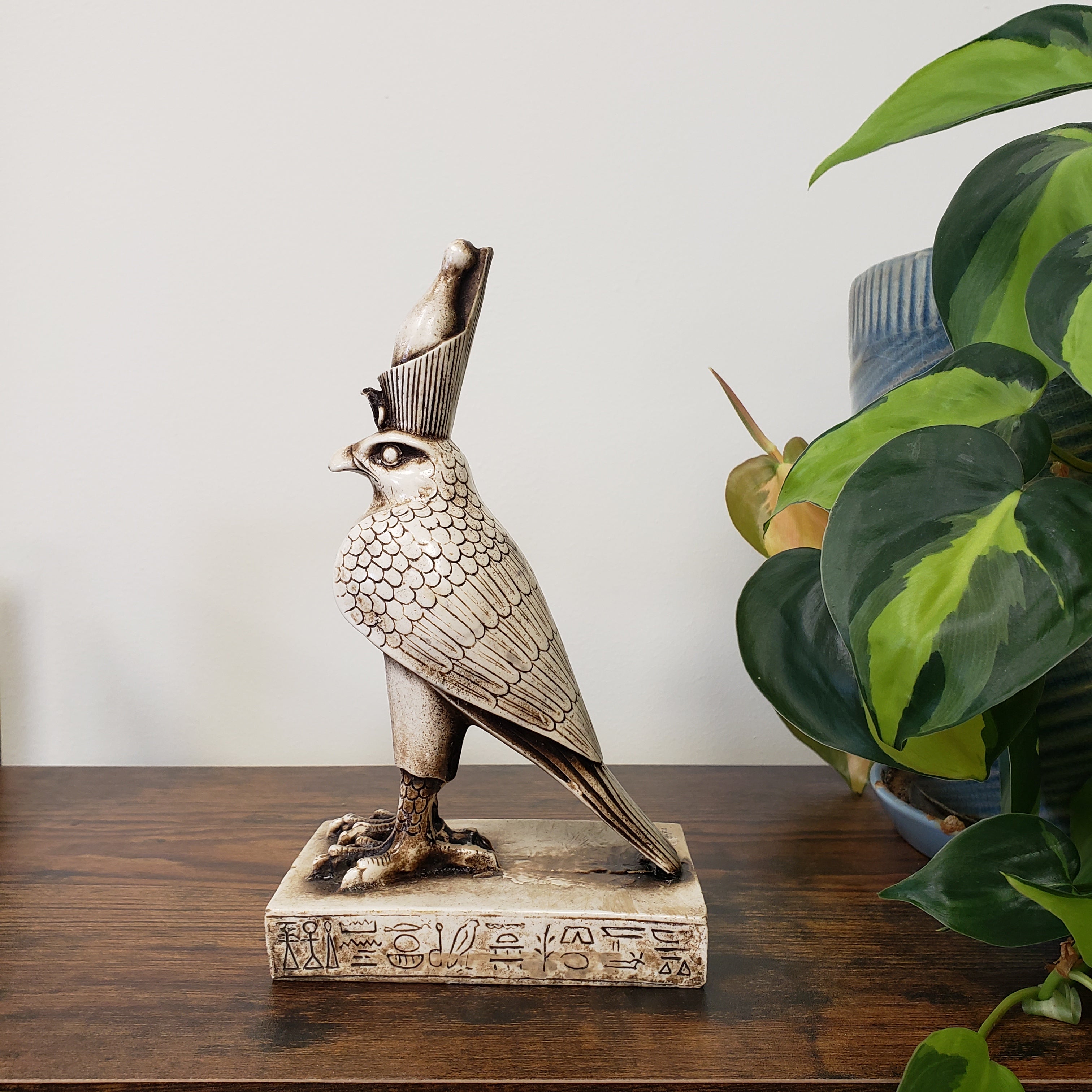 Egyptian falcon-god Horus sculpture on a wooden surface with a plant in the background