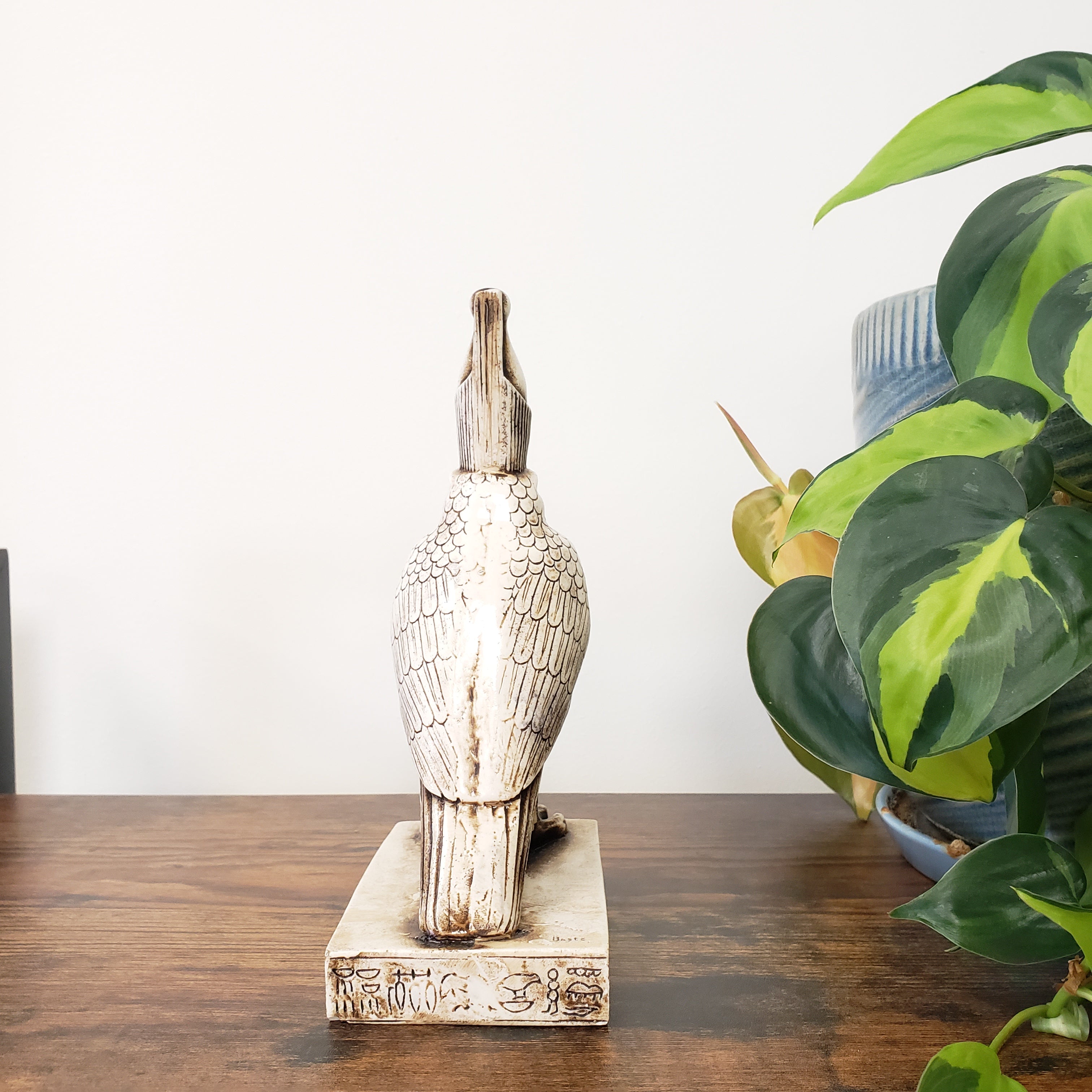 Decorative Egyptian falcon-god Horus statue on a wooden surface with a plant in the background