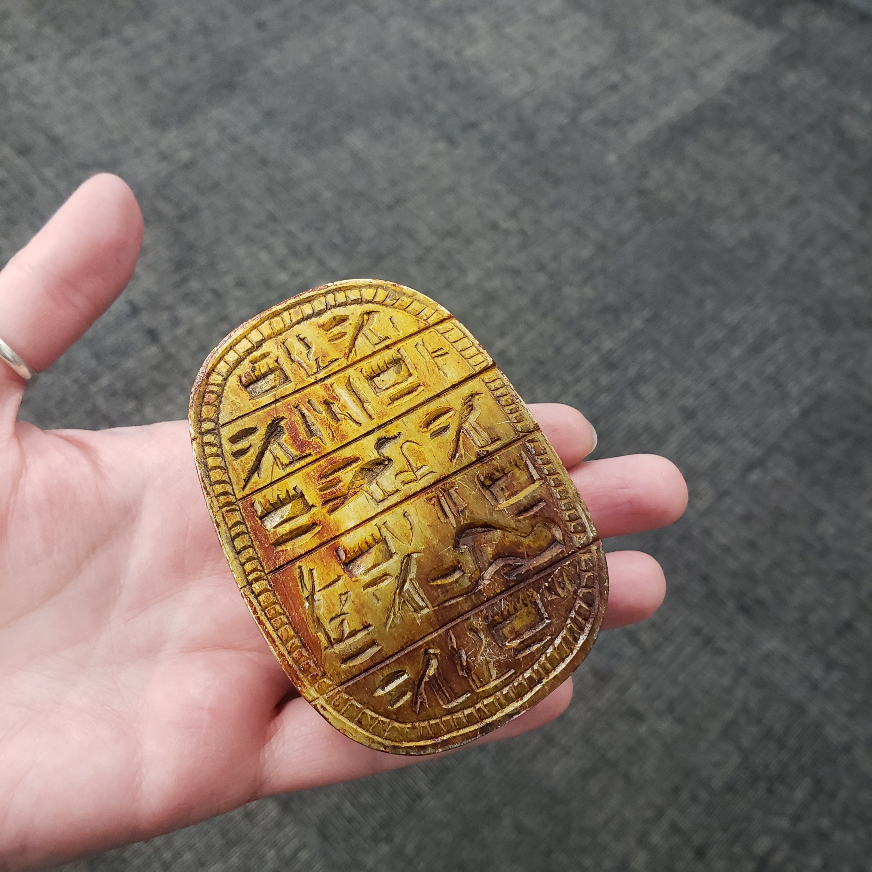 scarab statue with inscriptions held in a hand against a gray background