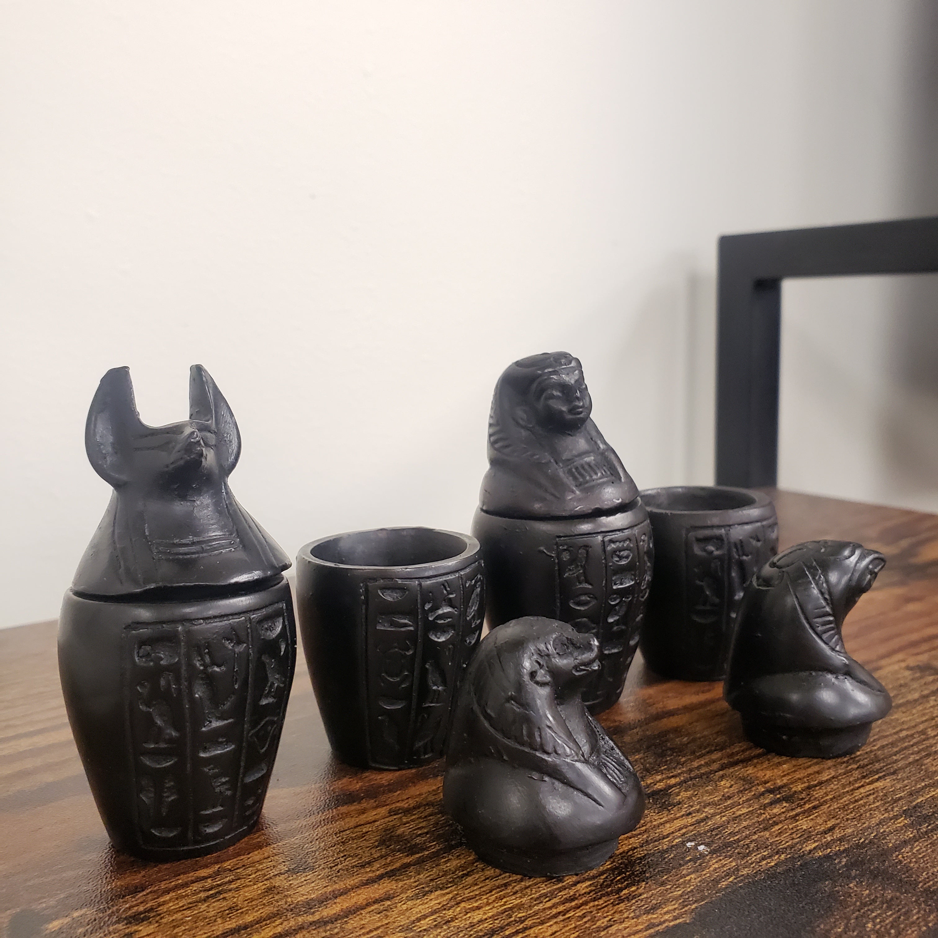 Set of black canopic jar statues with intricate designs on a wooden surface.