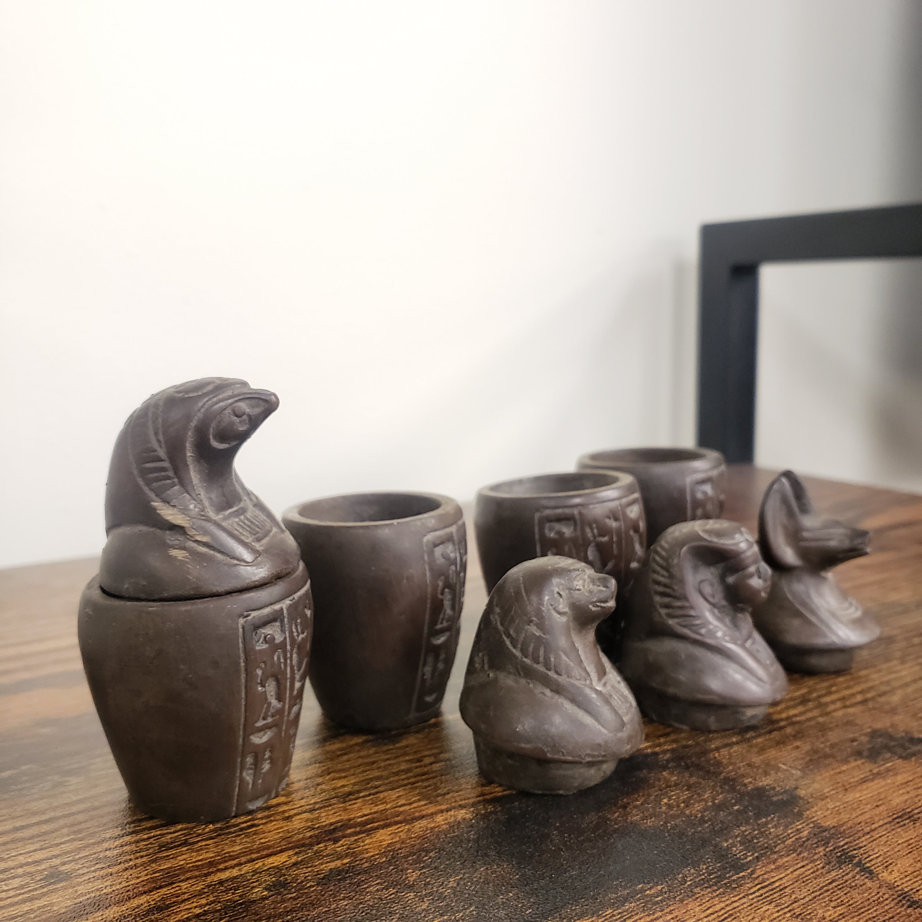 Set of dark brown canopic jar statues on a wooden surface