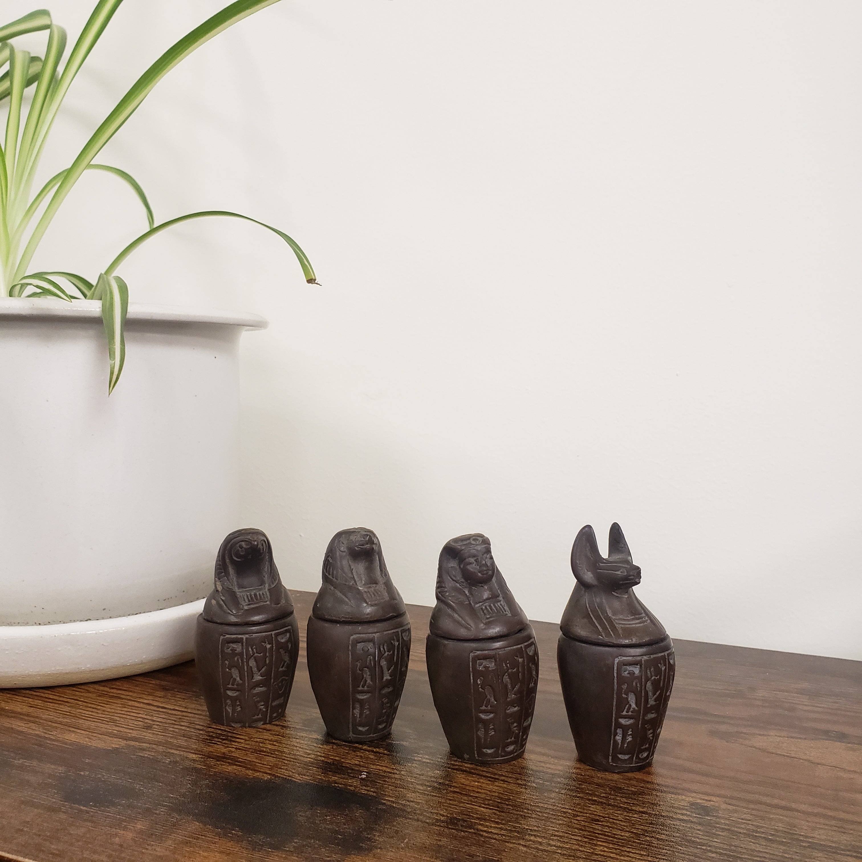 Four dark brown canopic jar statues on a wooden surface with a white background