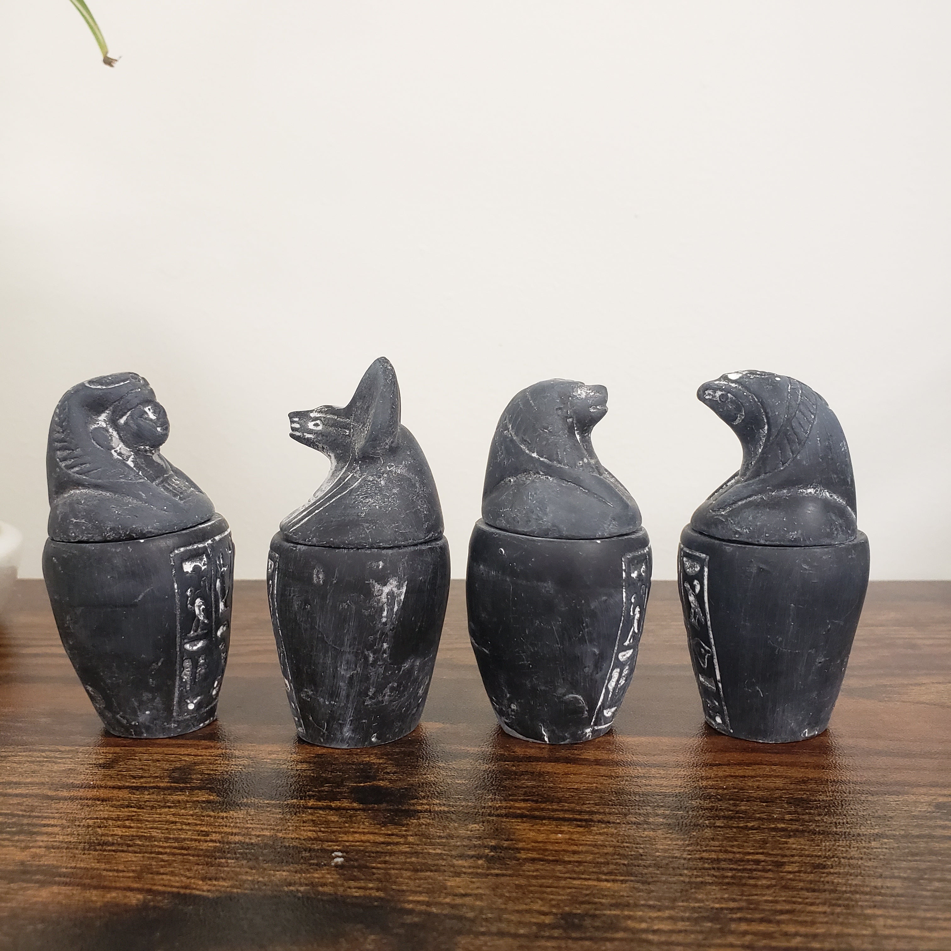 Four black canopic jar statues arranged on a wooden surface.