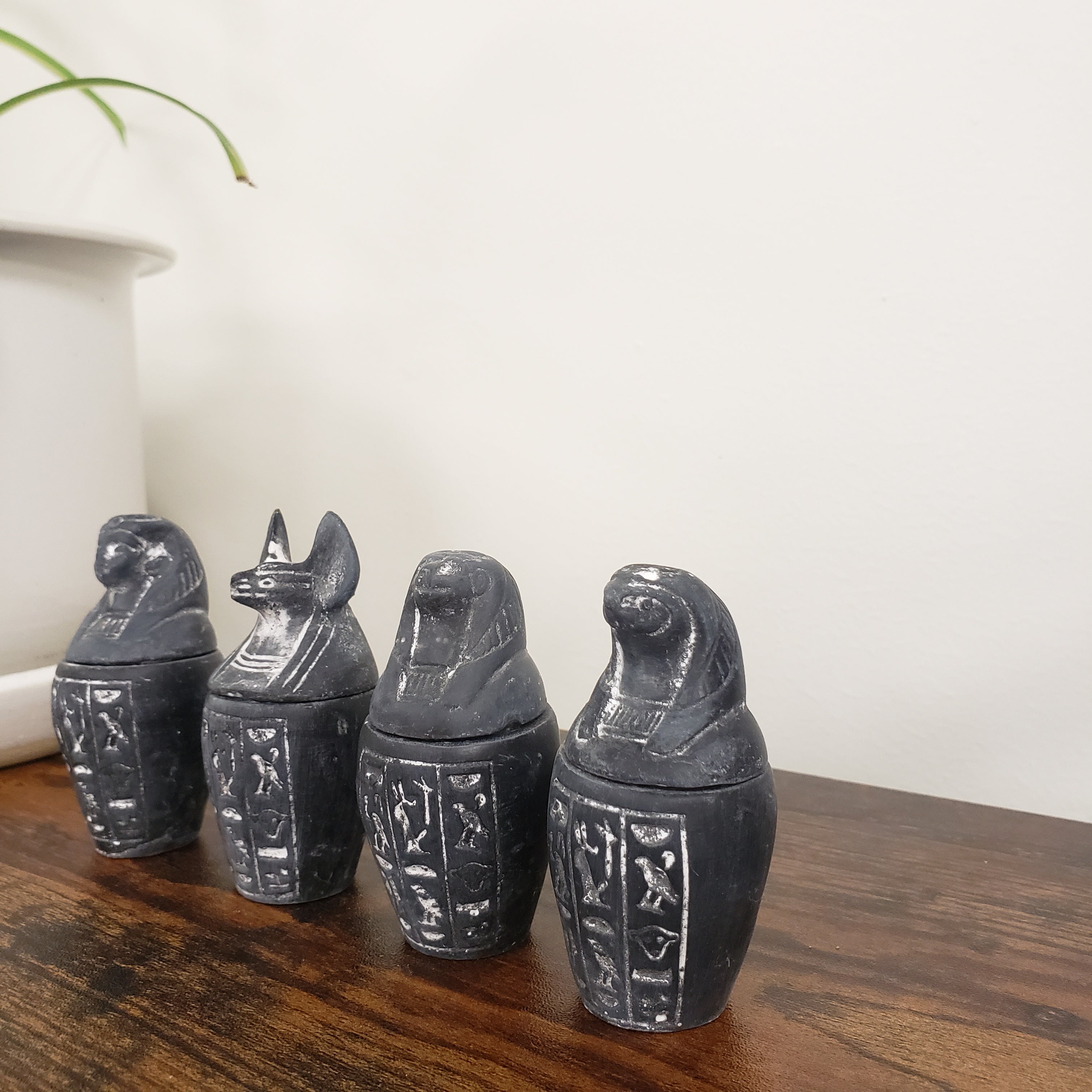 Set of four black canopic jar statues with hieroglyphic designs on a wooden surface.