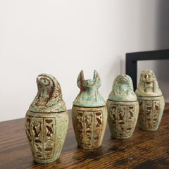 Set of four ancient Egyptian-style canopic jars with hieroglyphic designs on a wooden surface.