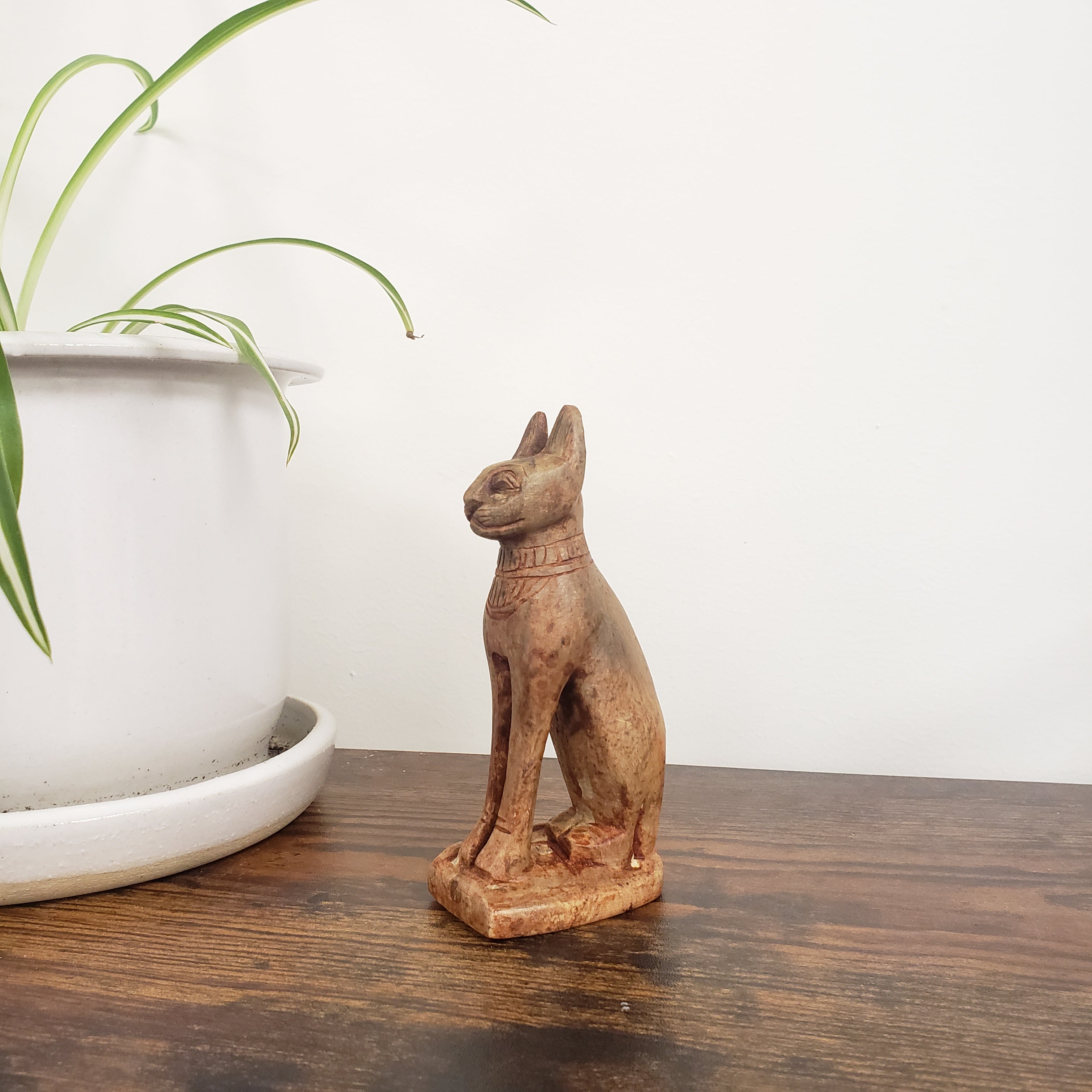 stone sculpture of a cat on a wooden shelf with a plant in the background
