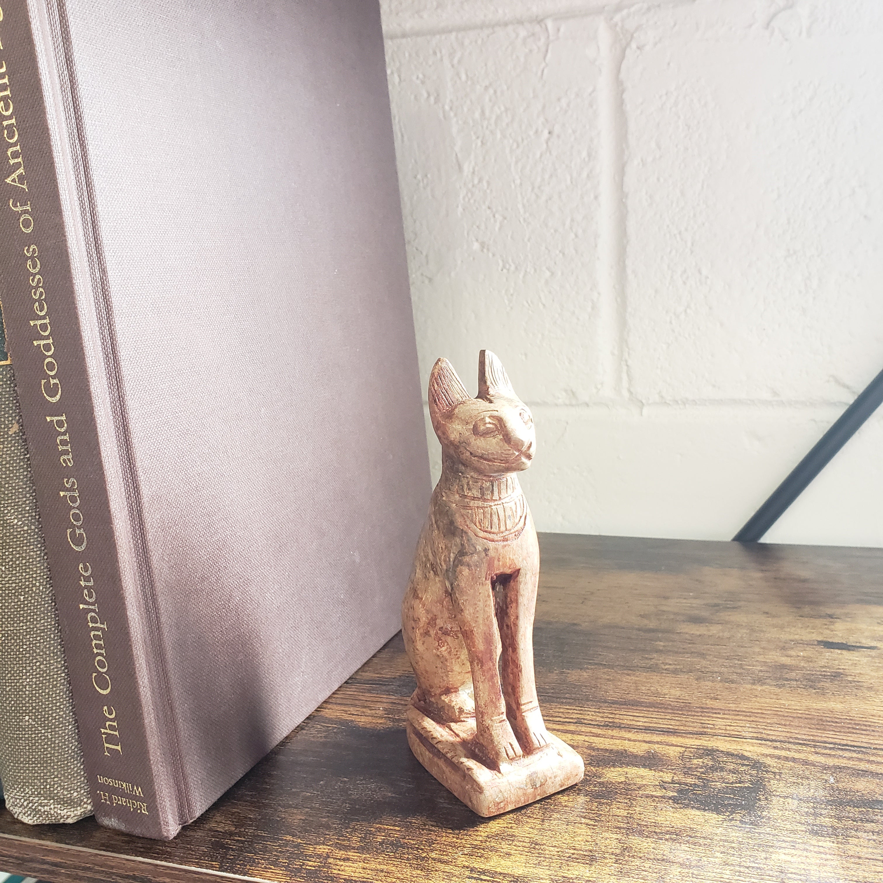 stone sculpture of a cat on top of a book titled 'The Complete Book of Cats' on a wooden shelf.