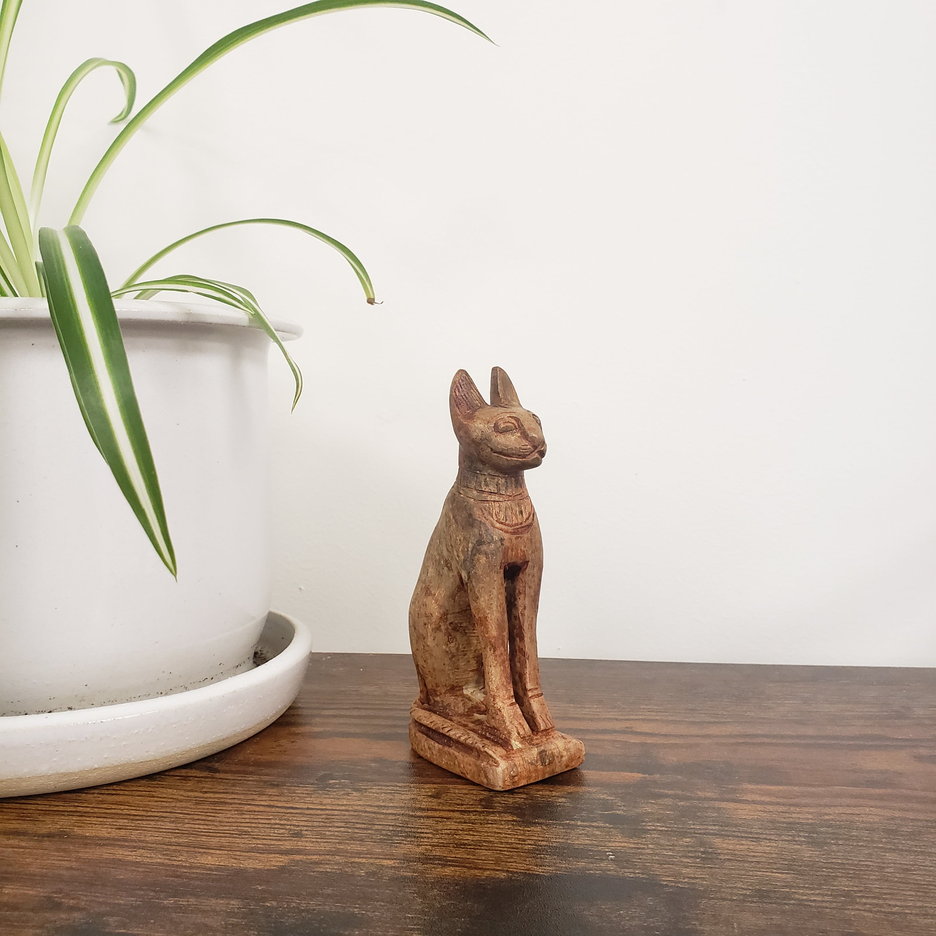stone cat figurine on a wooden shelf with a plant in the foreground
