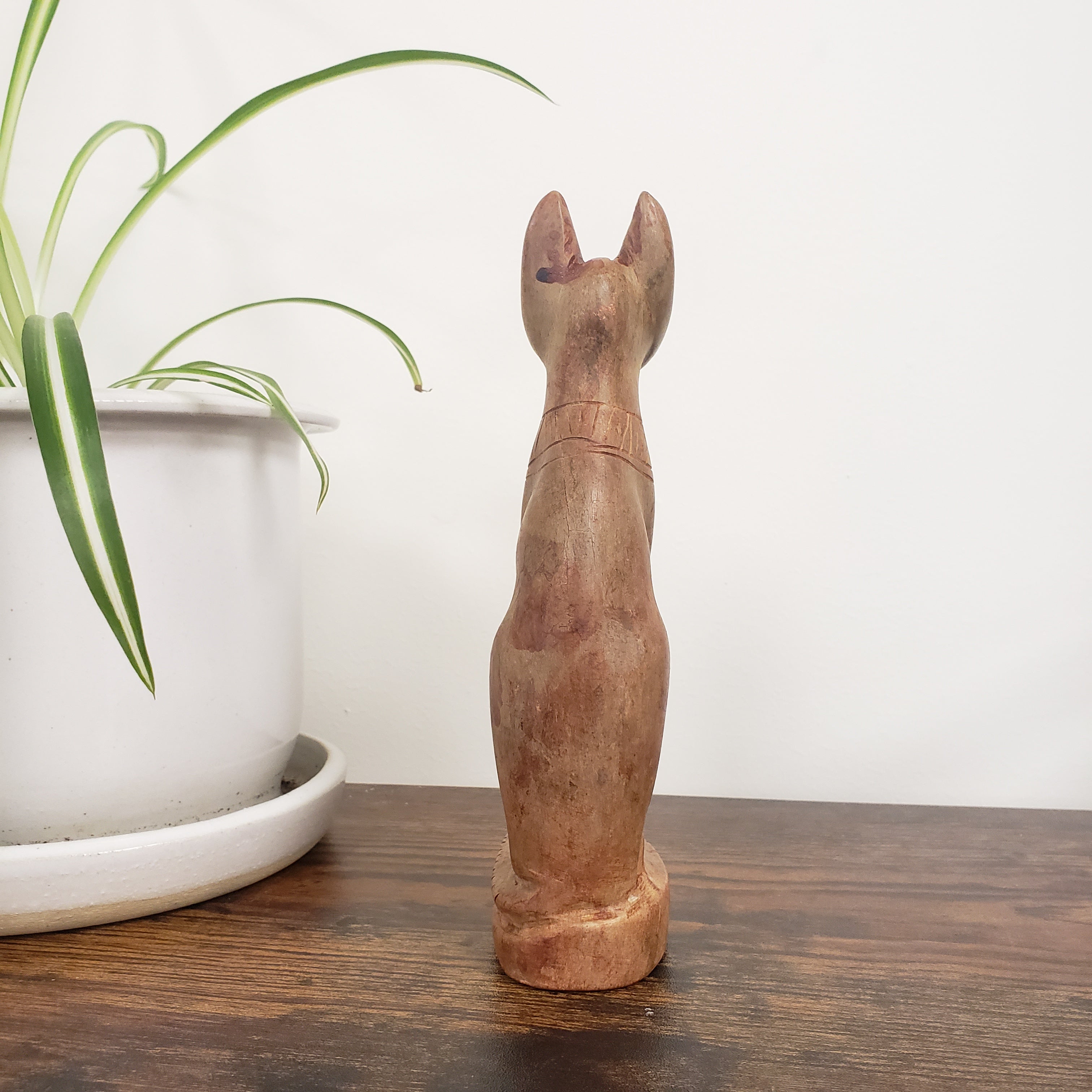 stone cat on a wooden shelf with a plant in the foreground.