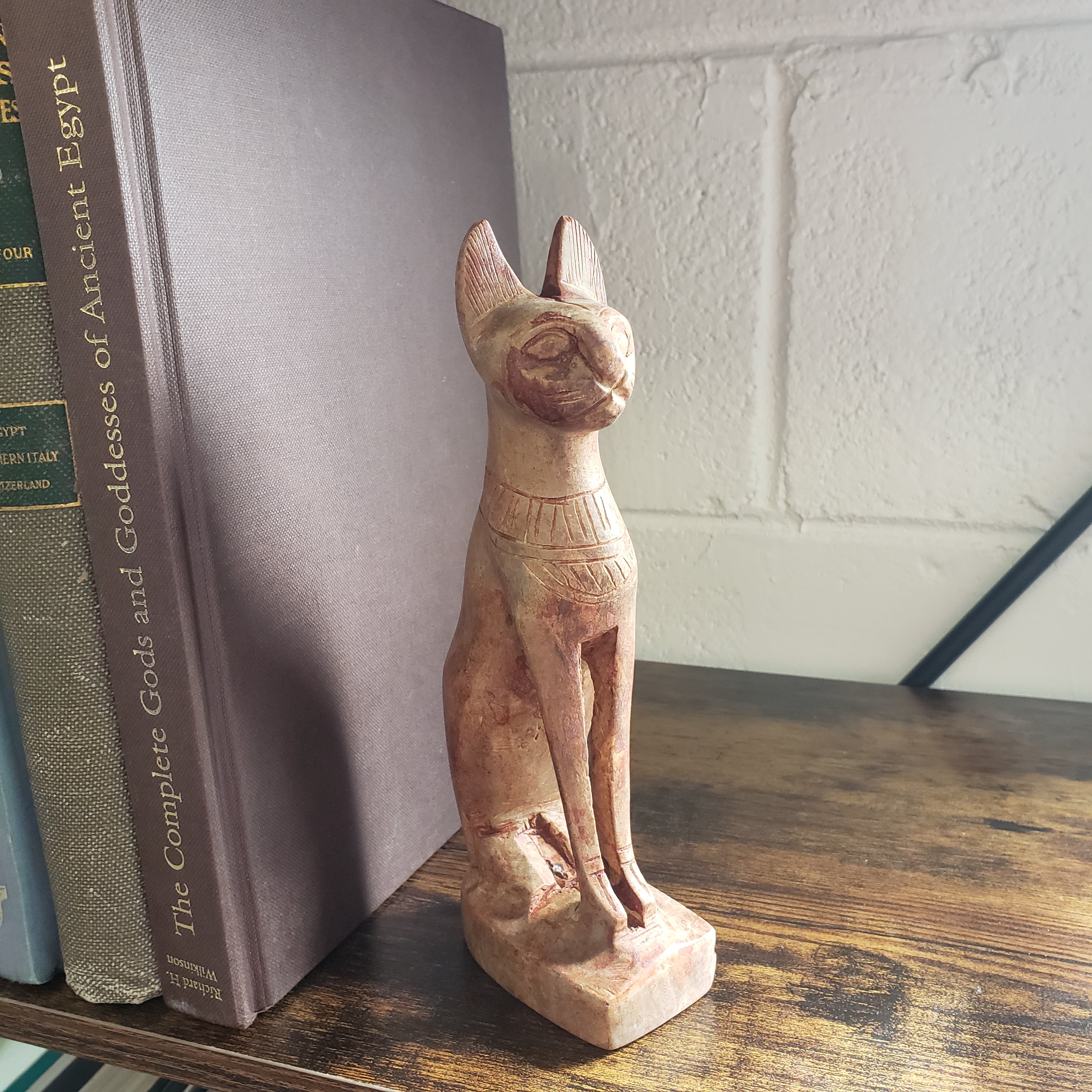 stone sculpture of a cat on top of books with a wooden shelf and white wall in the background