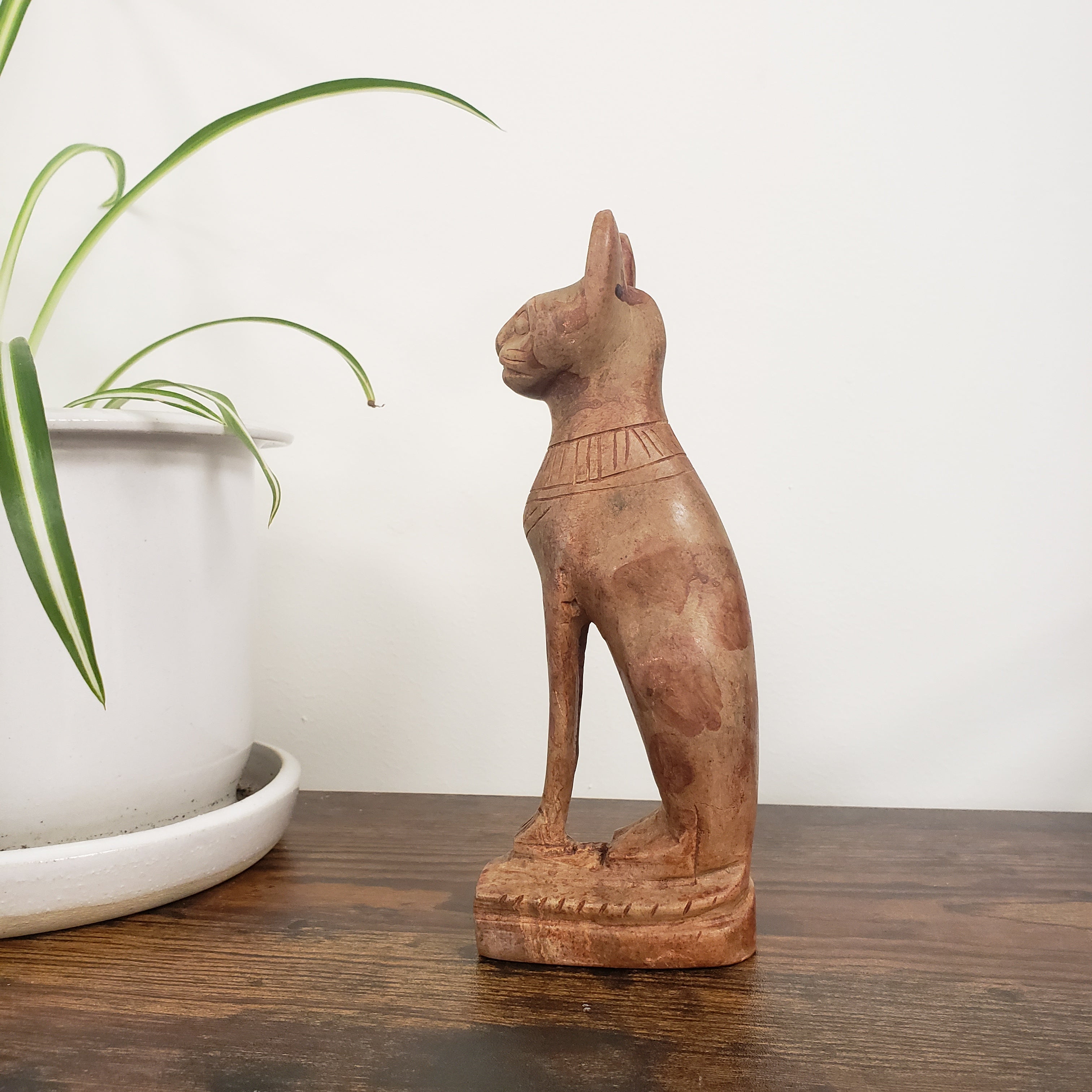 stone sculpture of a cat on a wooden surface with a plant in the background.