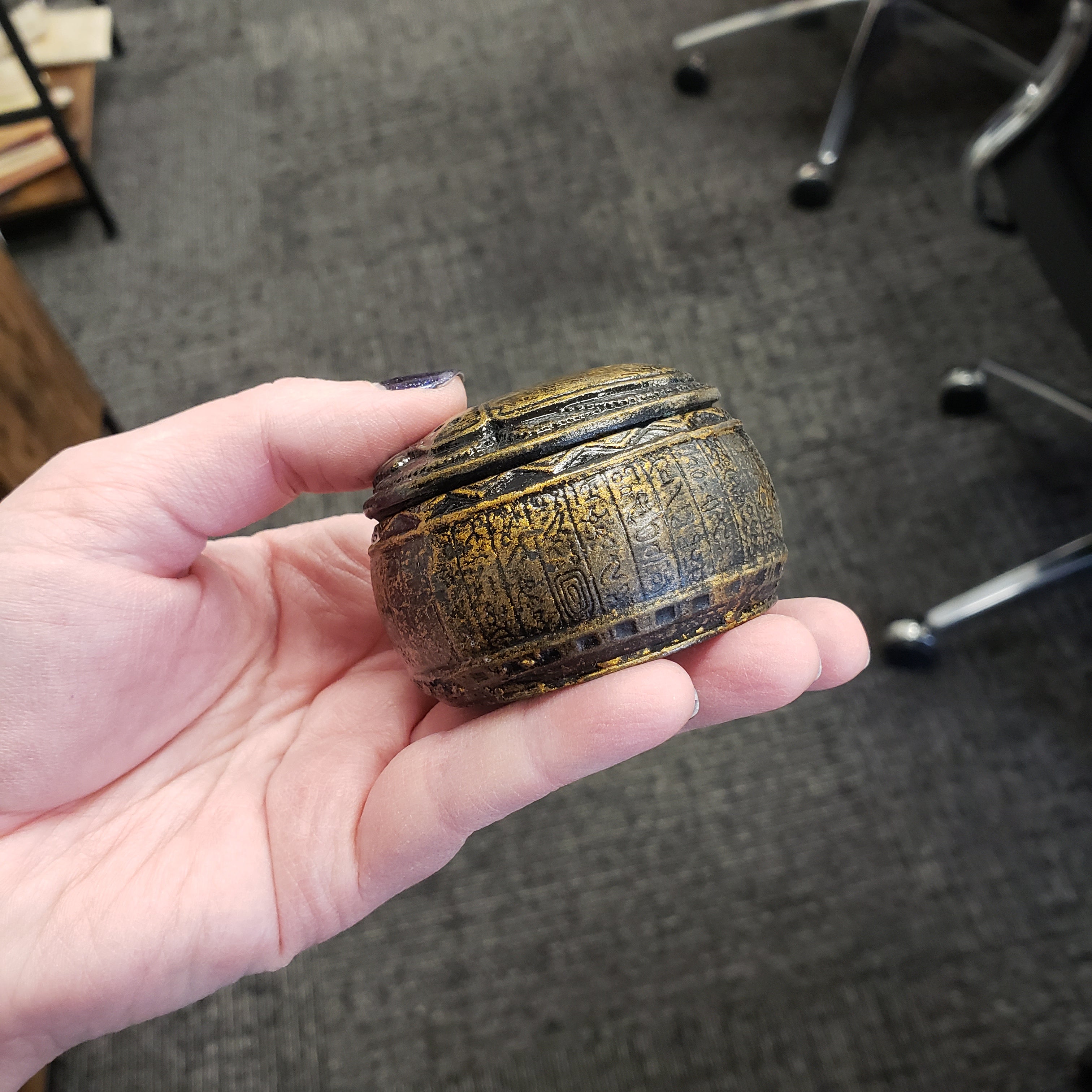 Hand holding a textured, round object with intricate patterns against a blurred indoor background