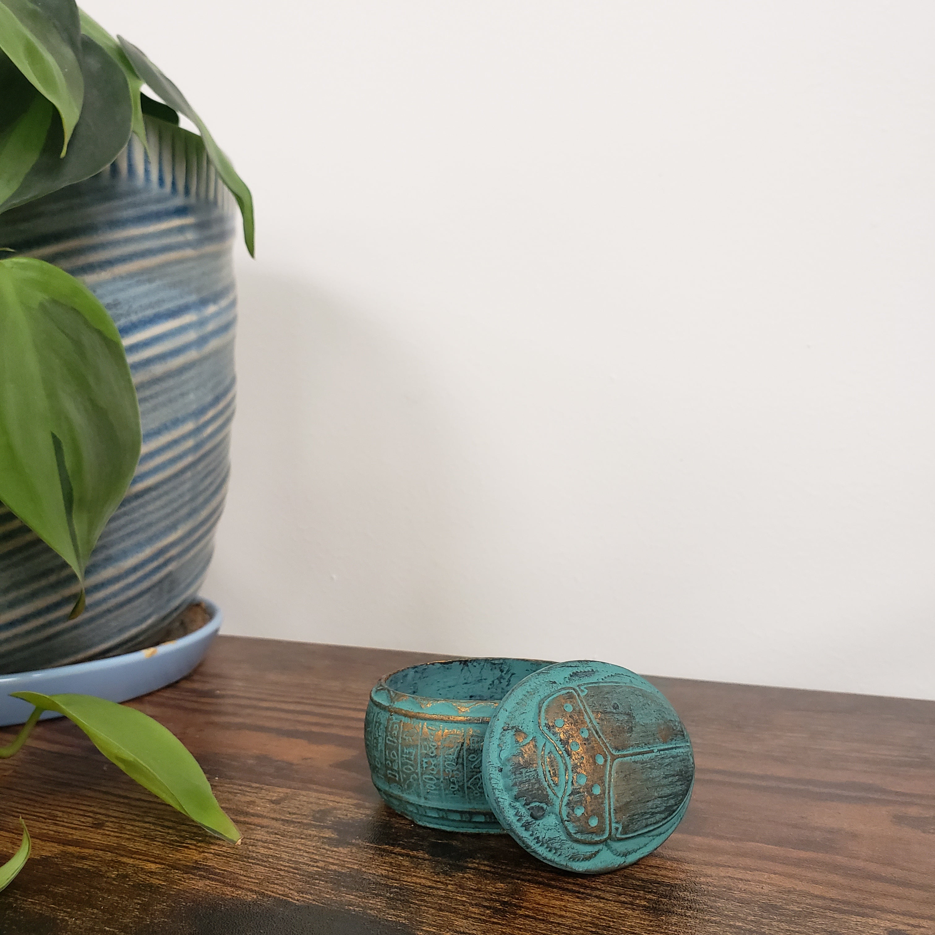 Decorative green Egyptian scarab box on a wooden door with plants in the foreground