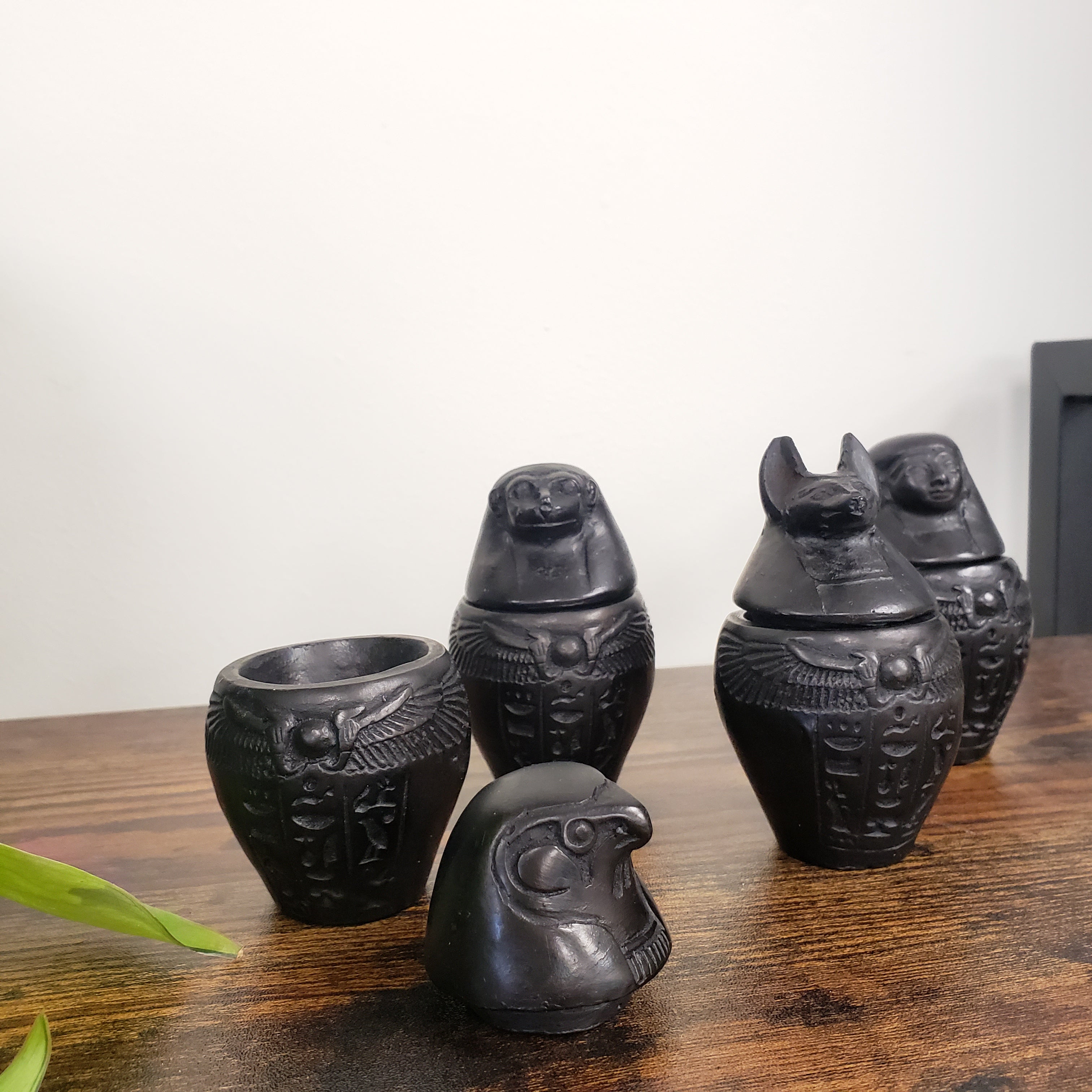 Set of black Egyptian-style canopic jars on a wooden surface with a white background