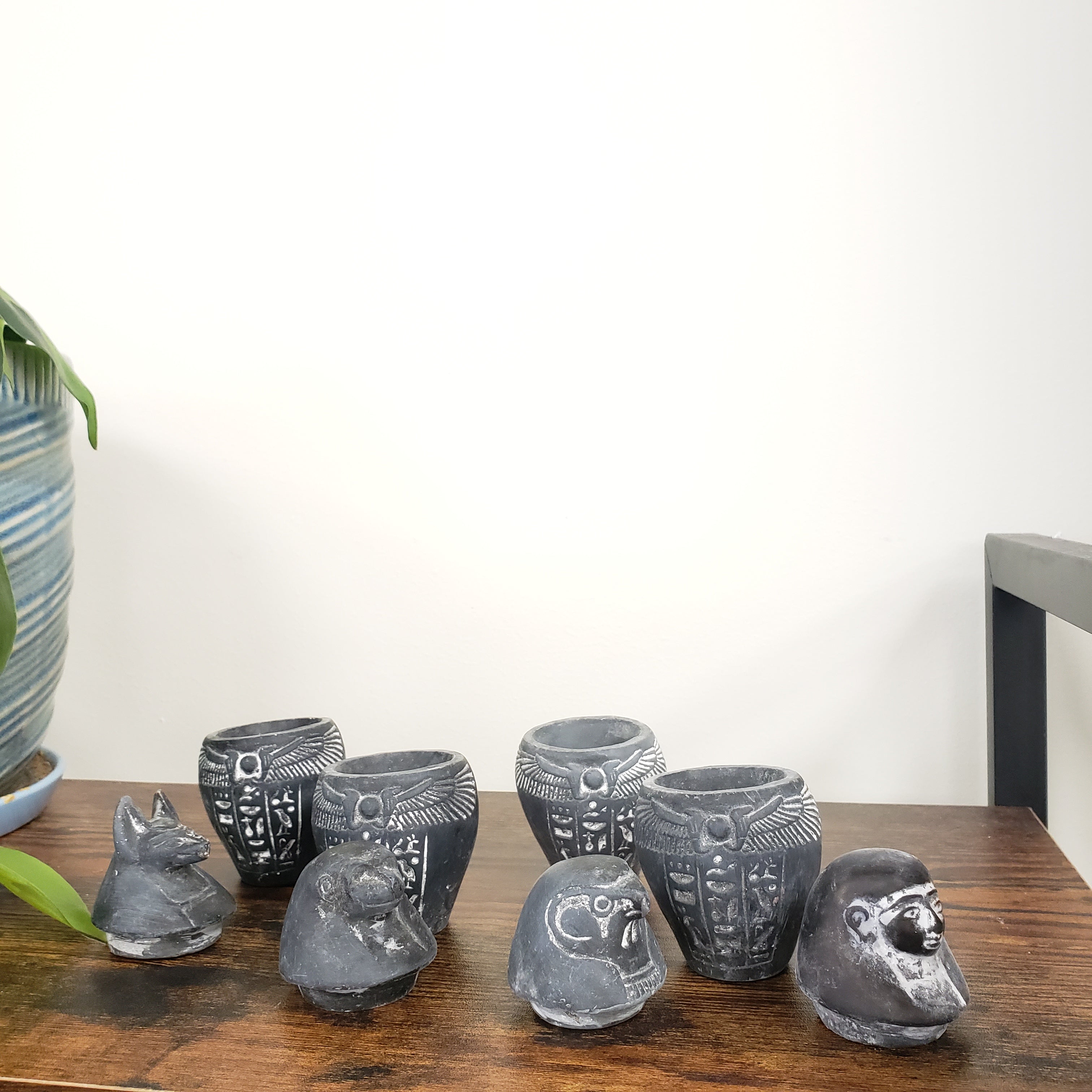 Decorative Egyptian-style canopic jars figurines on a wooden shelf against a white wall.