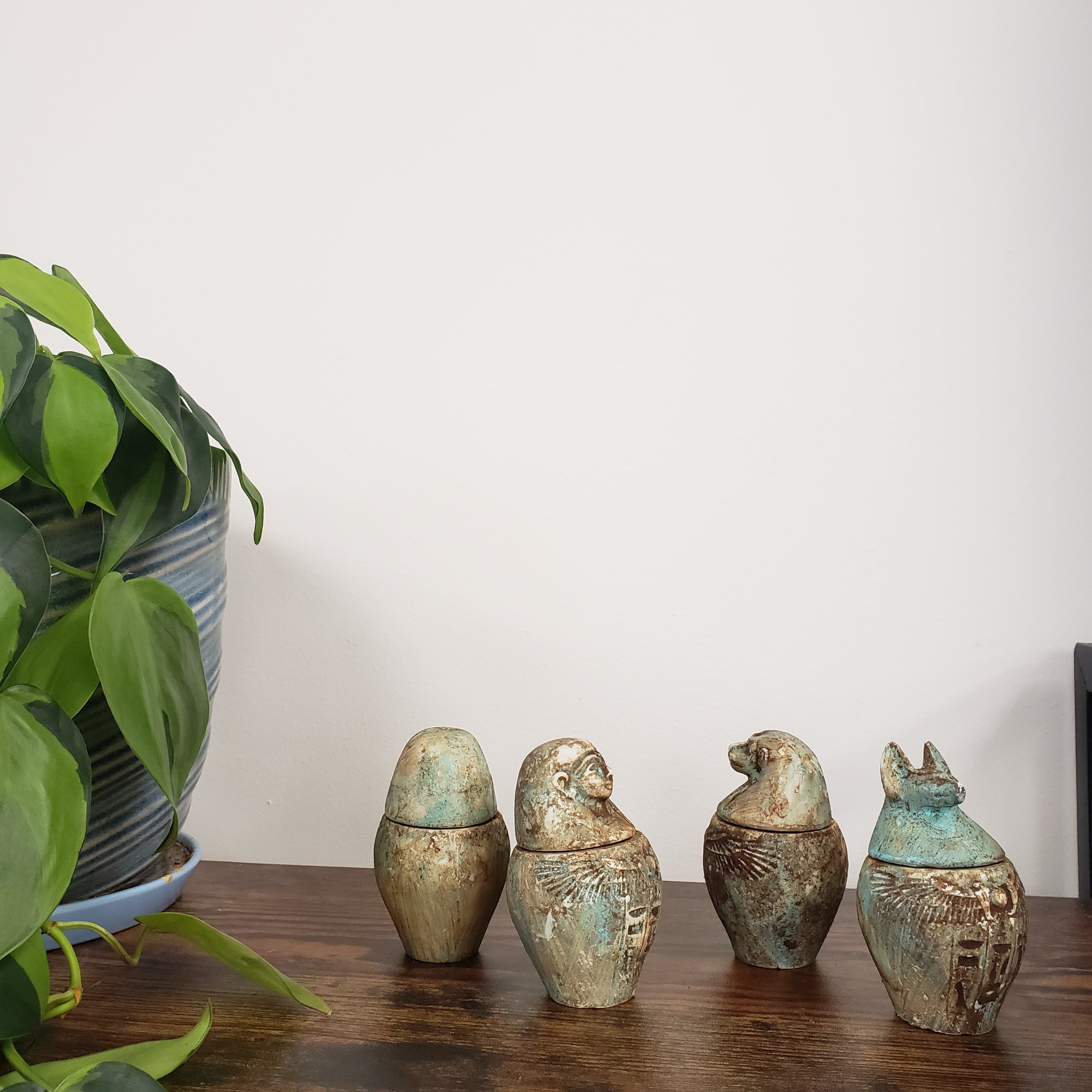 Decorative Egyptian-style canopic jars on a wooden board with a plant in the foreground