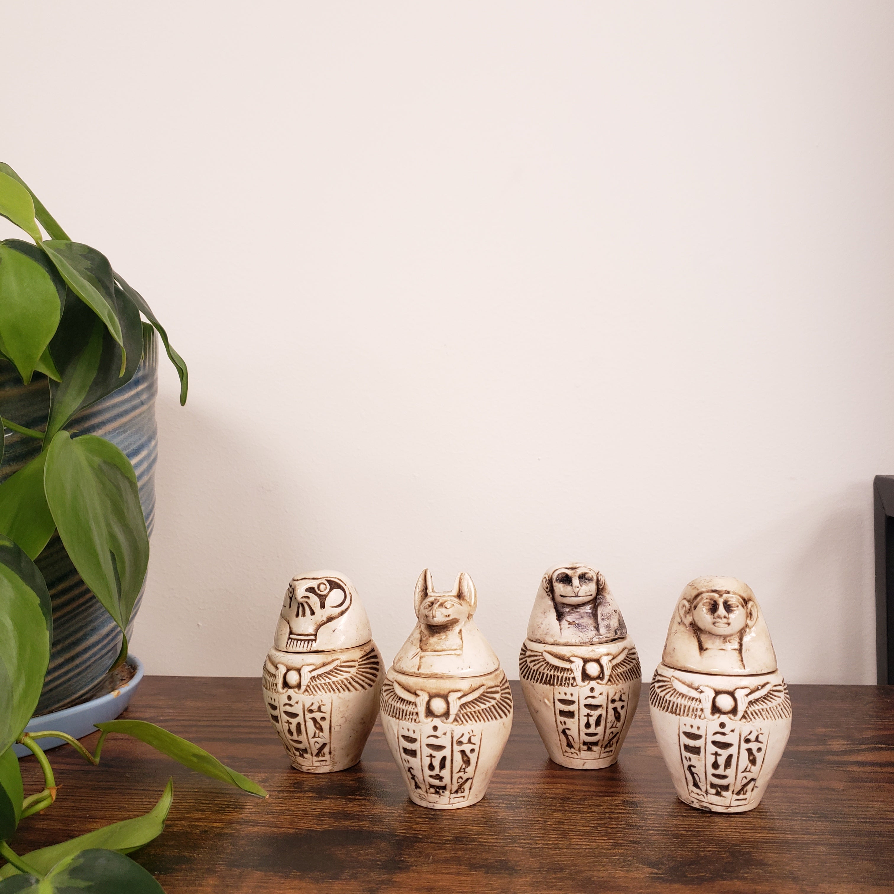 Egyptian-style canopic jar figurines on a wooden surface with a plant in the foreground
