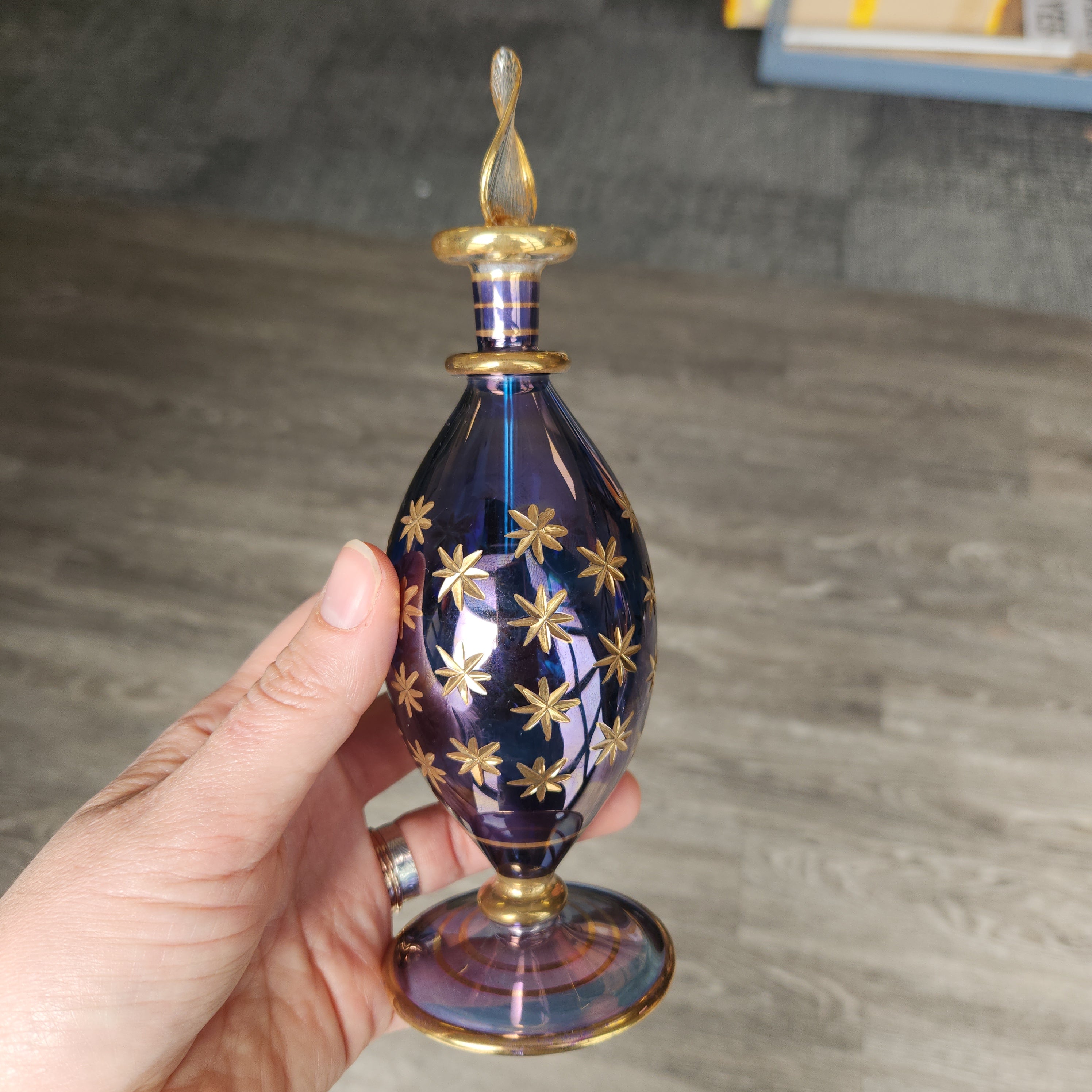Hand holding a decorative blue glass object with gold star patterns against a neutral background