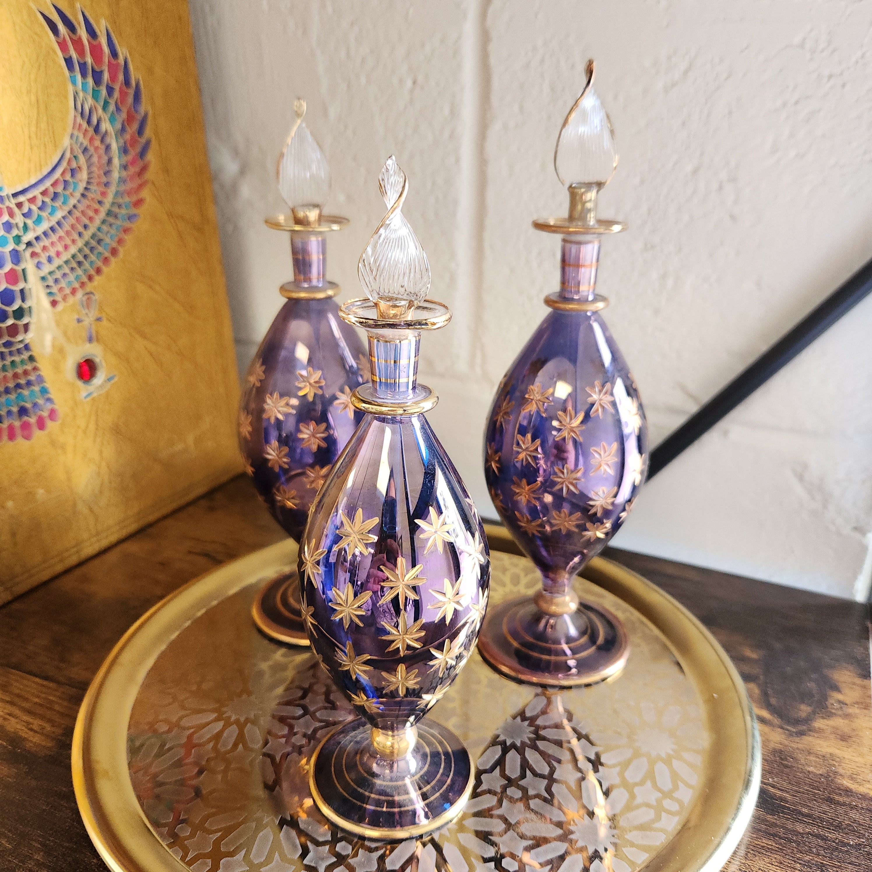 Decorative purple and gold glass bottles on a wooden surface with a colorful patterned rug.