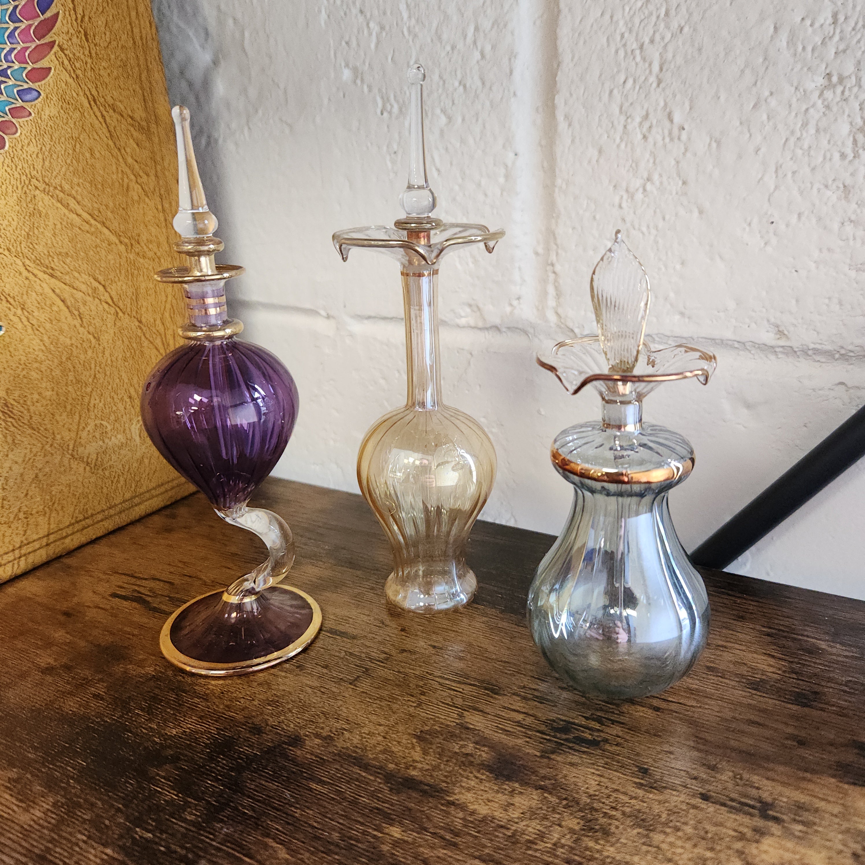 Set of three glass perfume bottles with different colored bulbs on a wooden surface.
