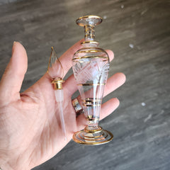 Decorative glass perfume bottles held in a hand against a gray background