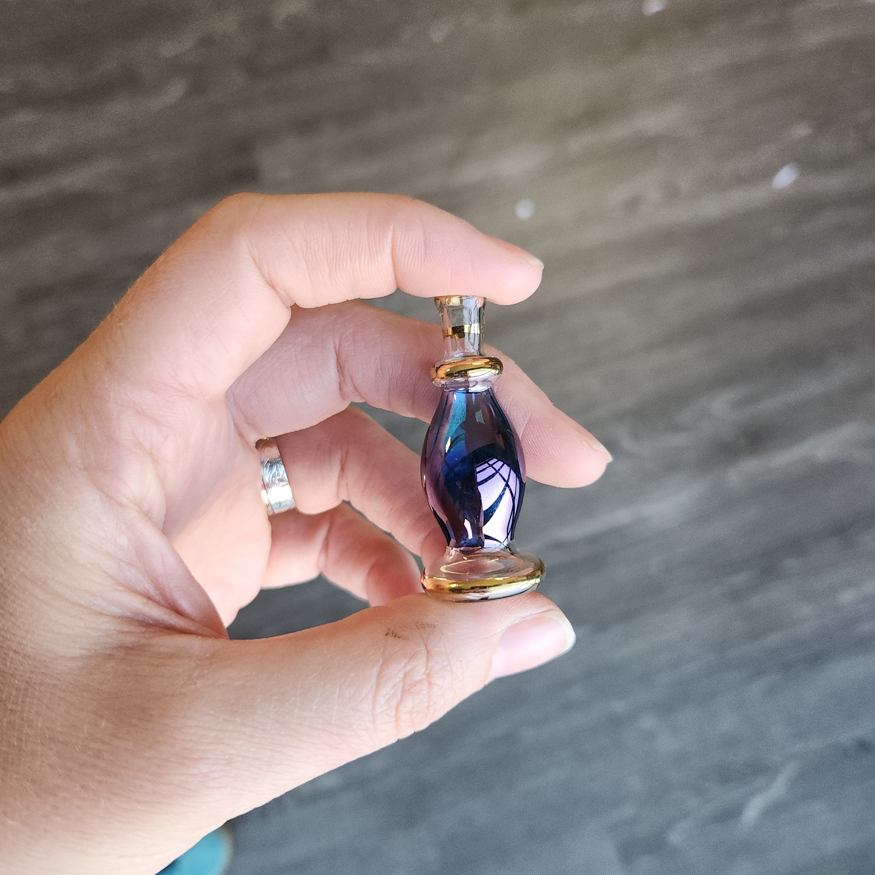 Hand holding a small purple and gold object against a gray background