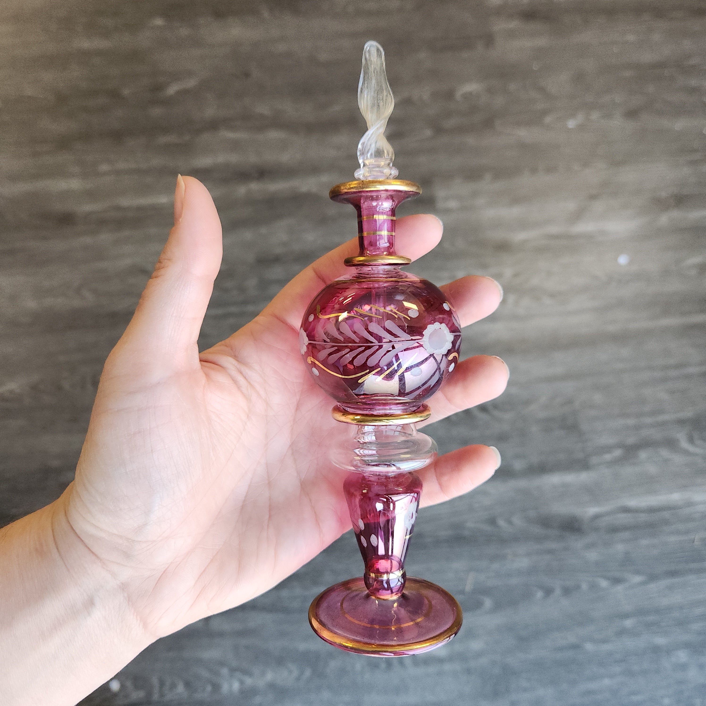 Hand holding a decorative glass bottle stopper against a wooden background