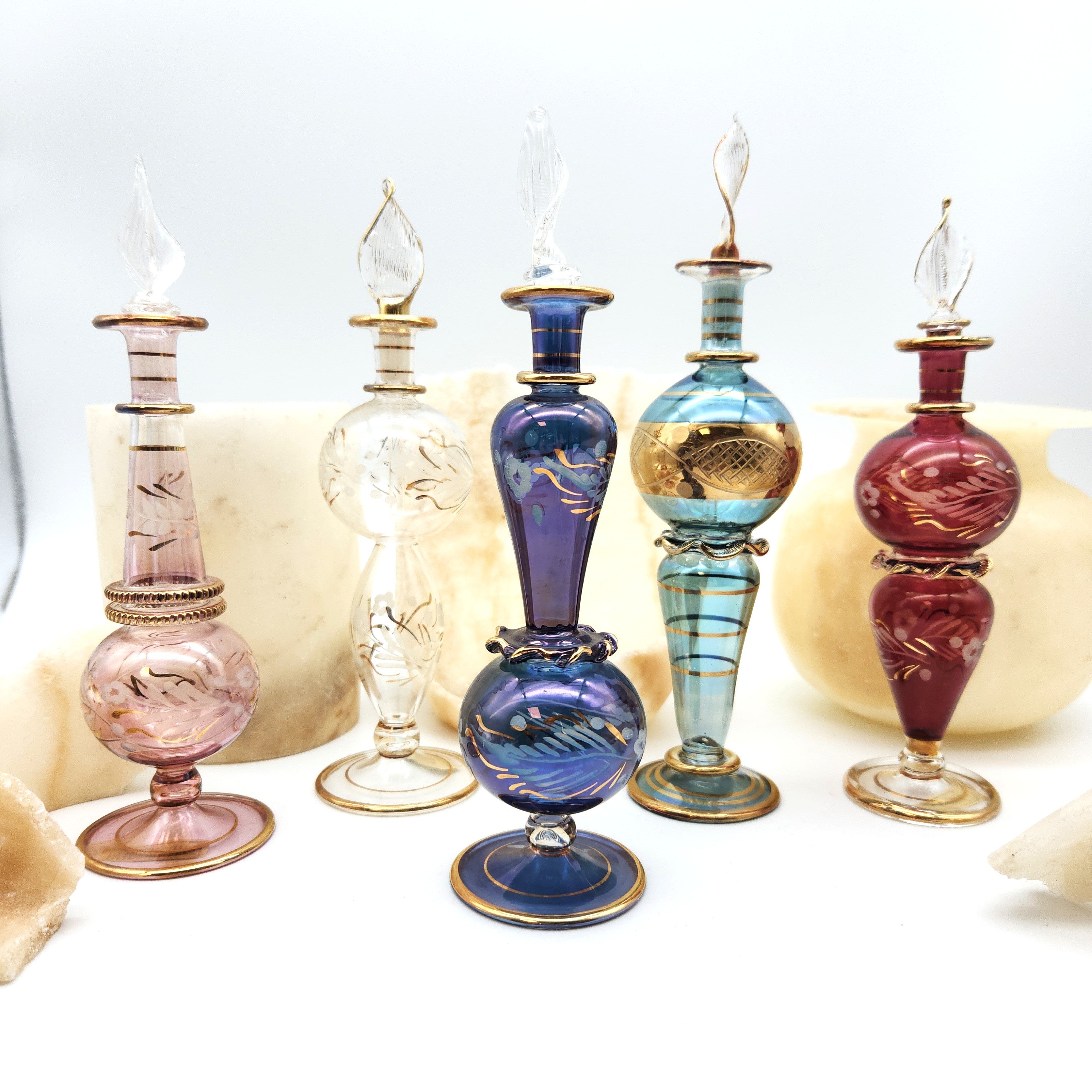 Set of colorful glass perfume bottles with decorative elements on a white background