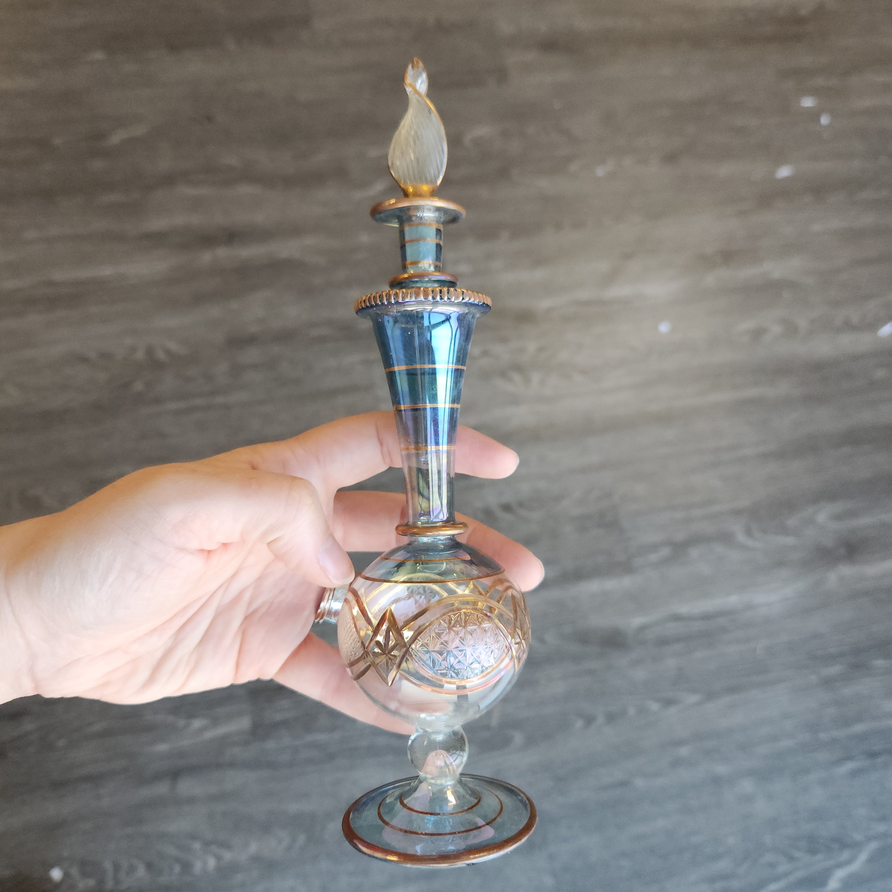 Decorative glass bottle held by a hand against a gray background