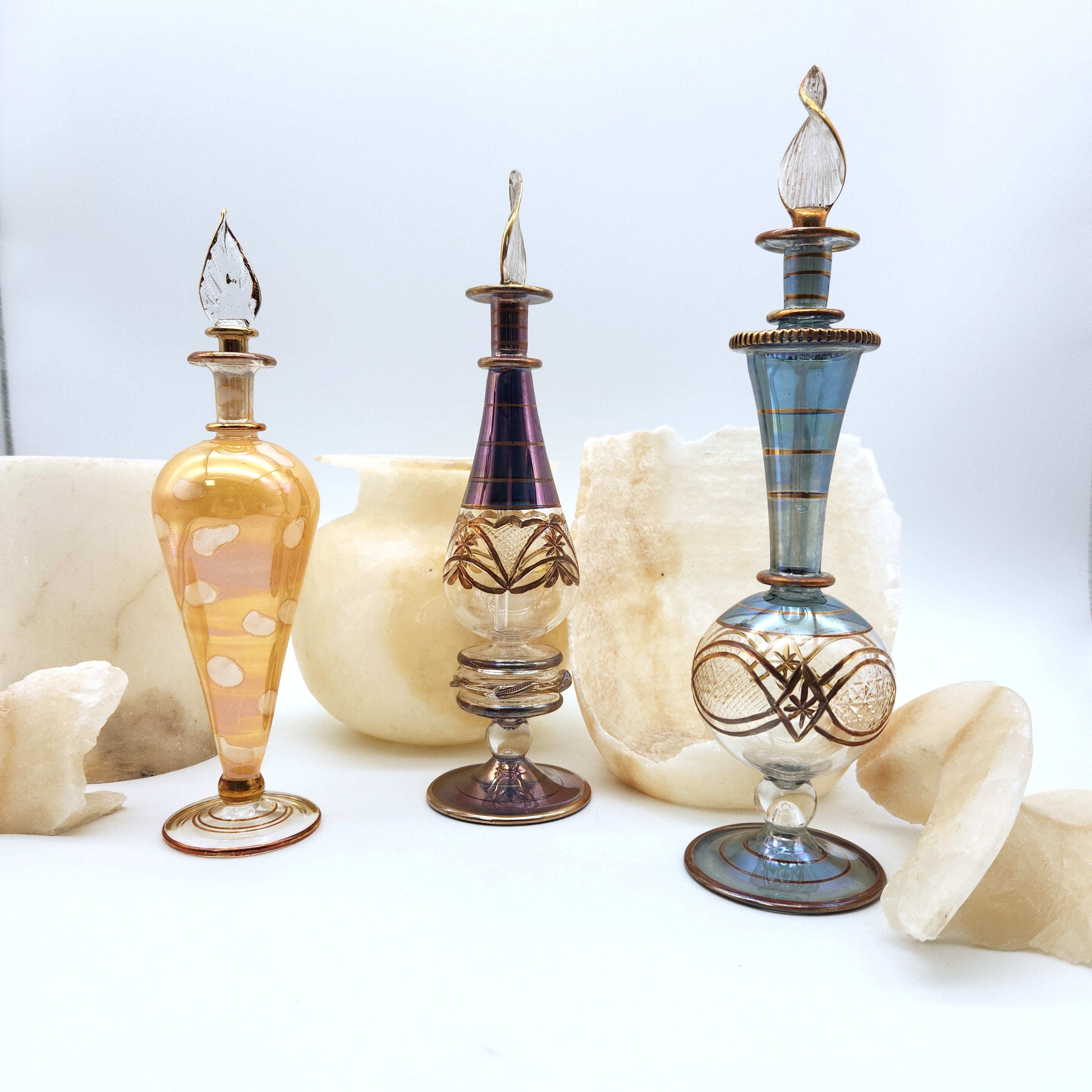 Three ornate glass bottles with decorative designs on a white surface.