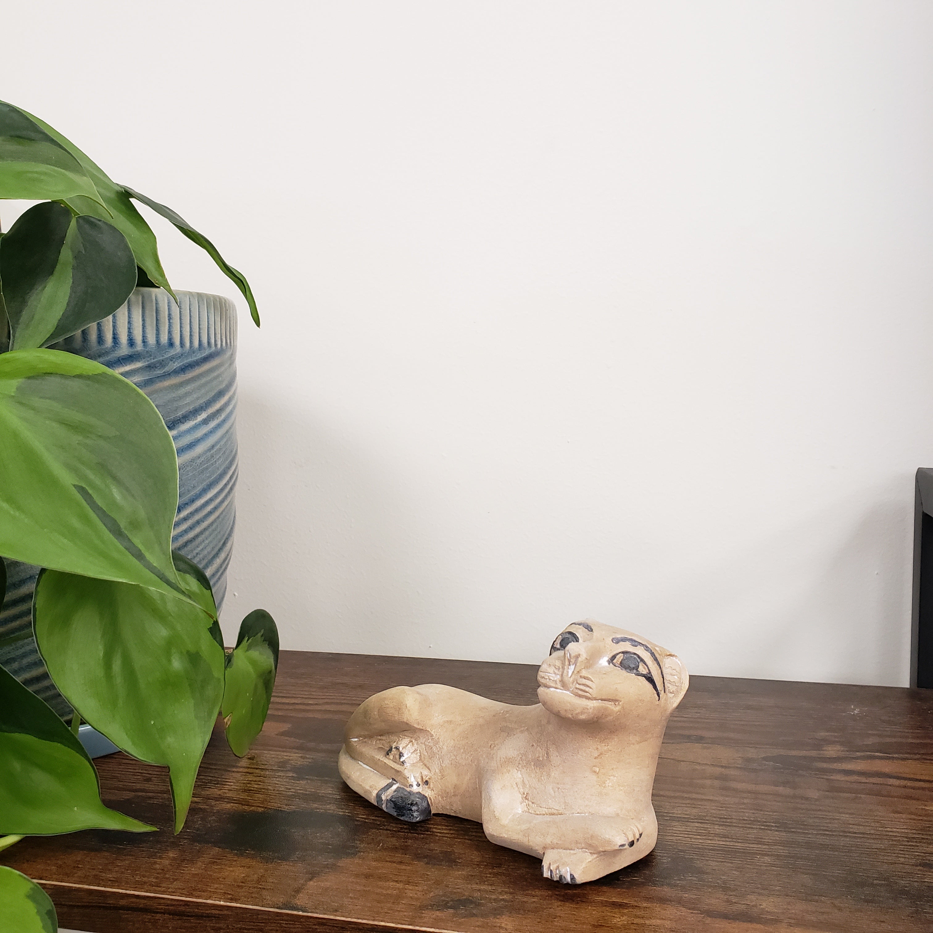 Decorative stone lion sculpture on a wooden board with a plant in the foreground.