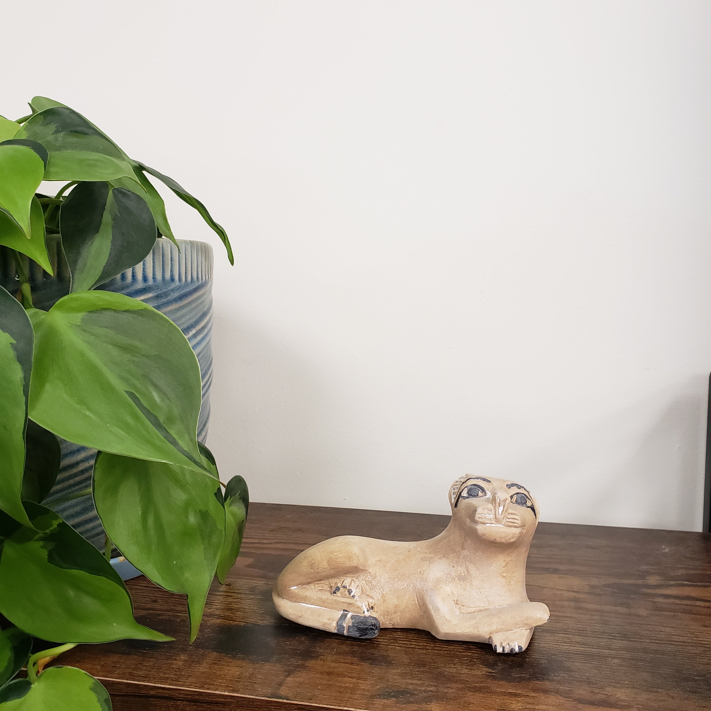 Decorative stone sculpture of a lion on a wooden board with green plants in the foreground.