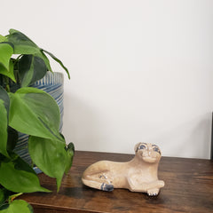 Decorative stone sculpture of a lion on a wooden board with green plants in the foreground.