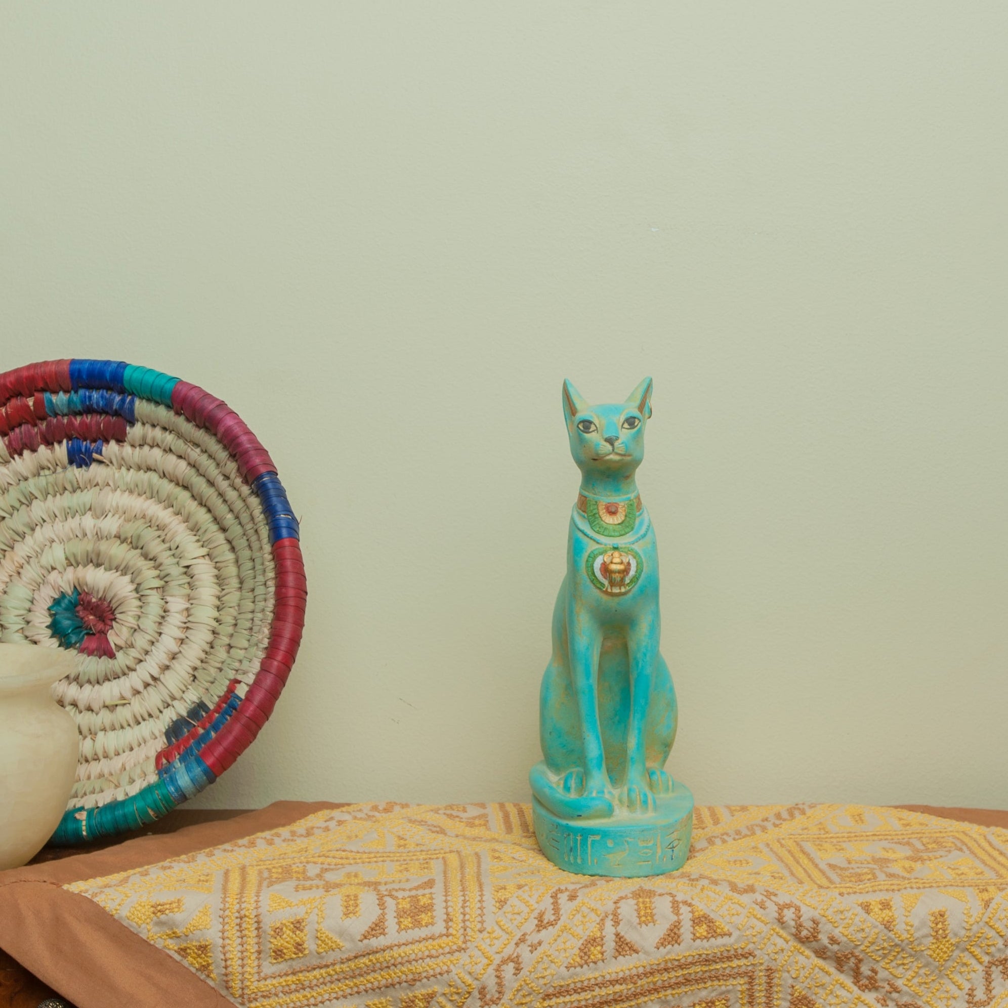 Decorative items including a turquoise cat figurine, woven basket, and ceramic vase on a wooden surface with a light green wall in the background.