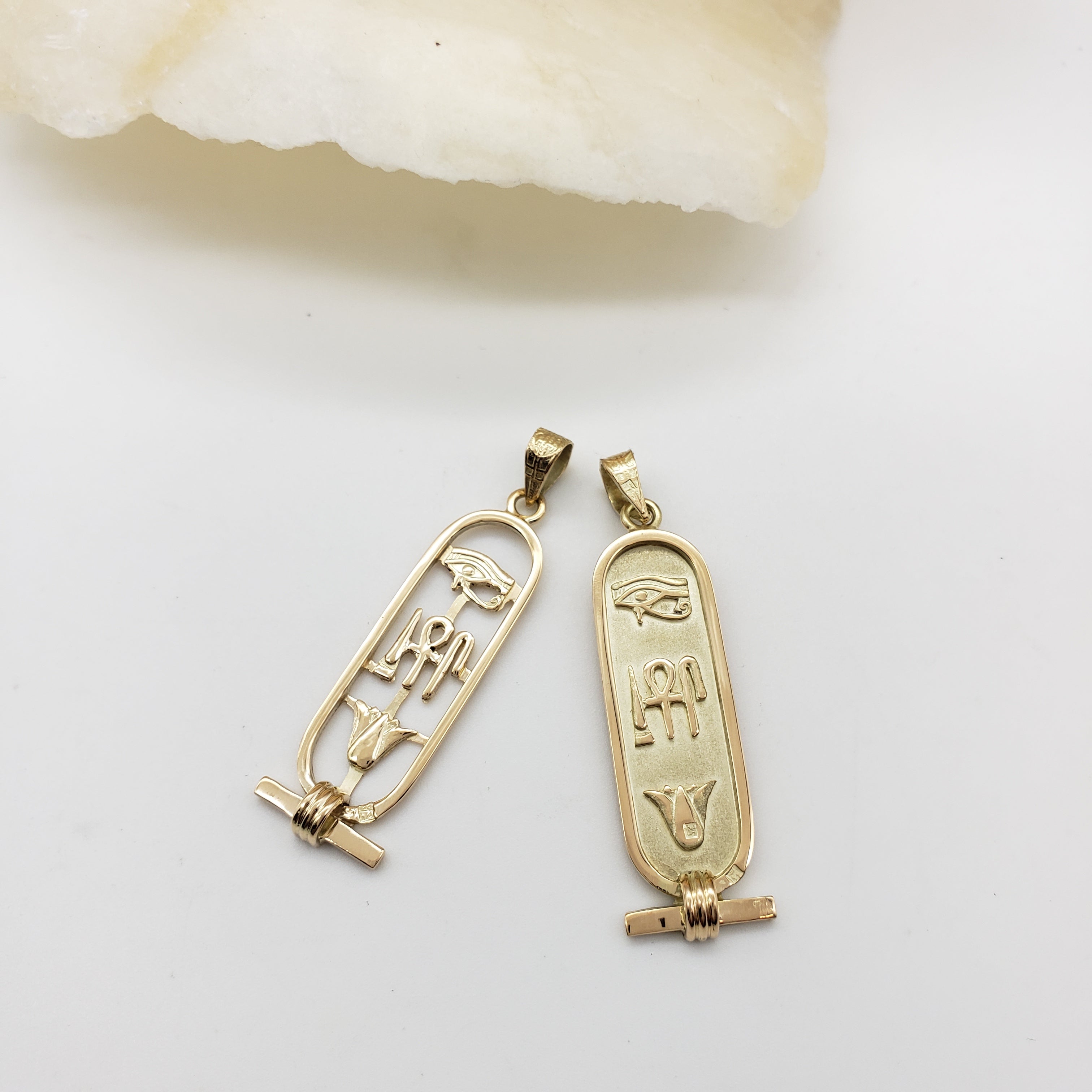 Two gold pendants with hieroglyphic designs on a light background