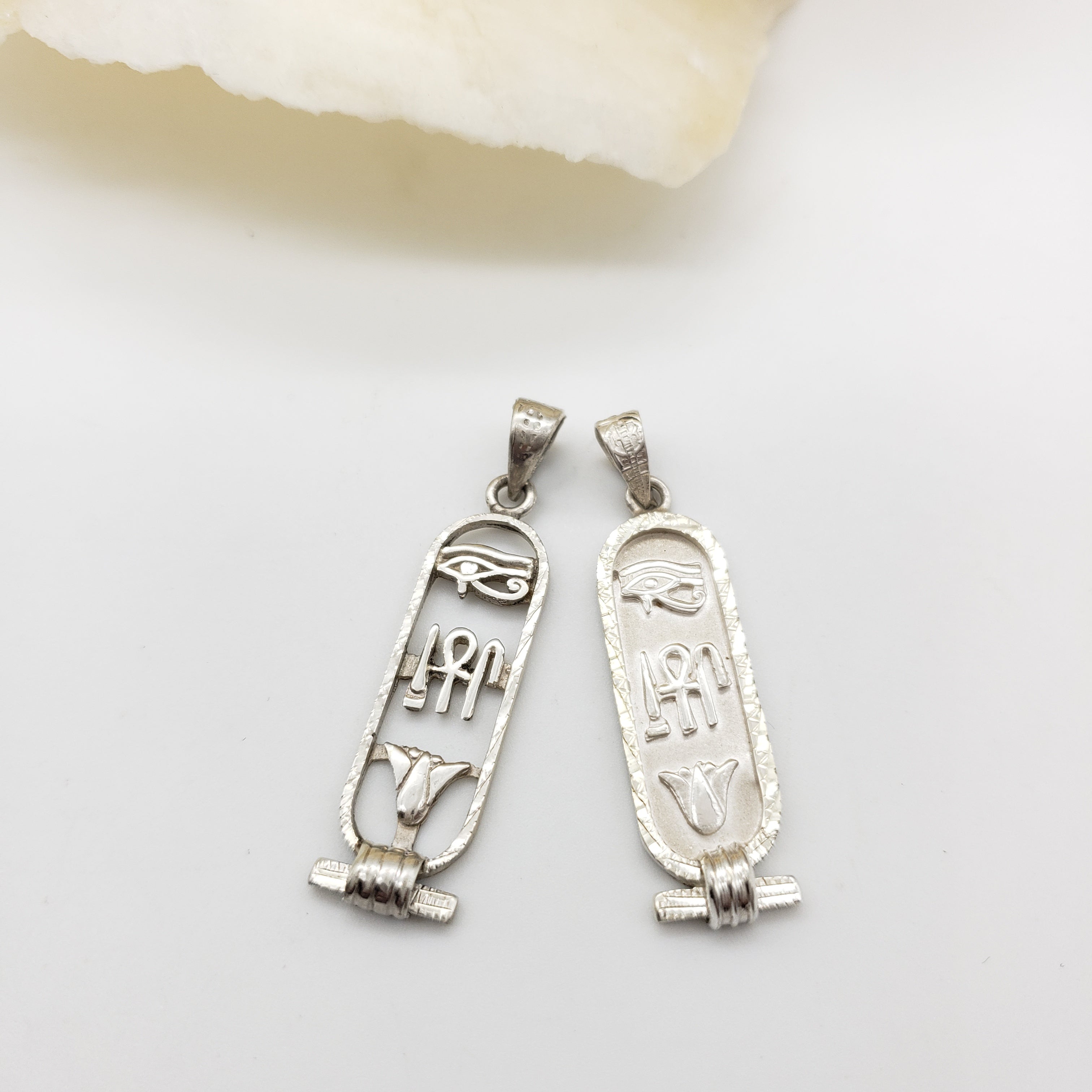 Two silver hieroglyphic pendants on a white background