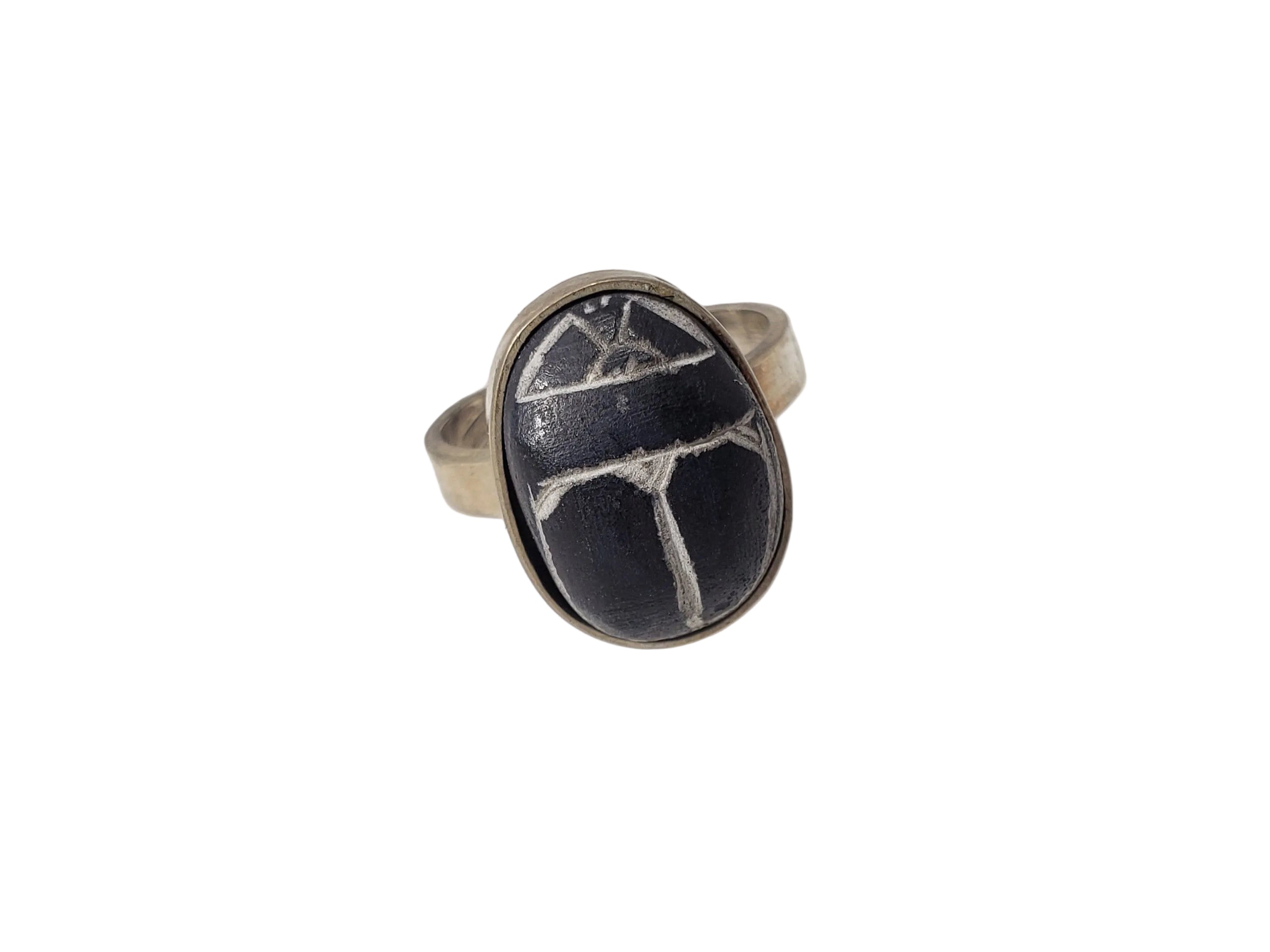 An Egyptian black and white scarab ring made of silver, displayed on a white surface.