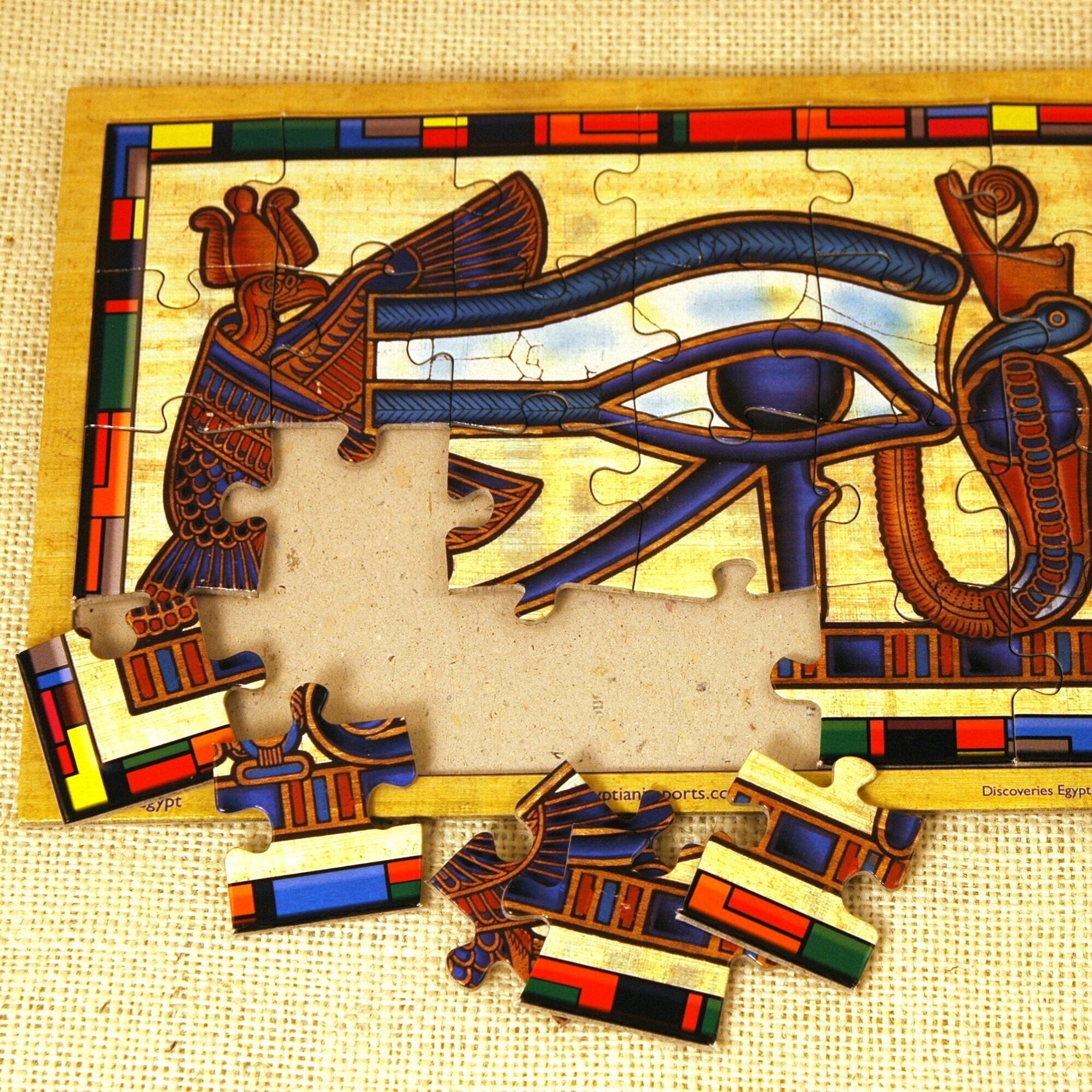 A colorful jigsaw puzzle piece featuring an ancient Egyptian Udjat Eye symbol with a missing piece, set on a beige background.