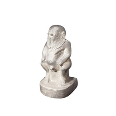 A hand-carved stone statue of the Egyptian God Bes, depicted as a dwarf with large ears, a long-haired and bearded figure, holding a rattle.