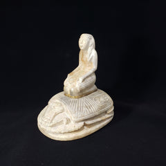 A hand-carved stone sculpture of an Egyptian scarab with a seated pharaoh on top, featuring hieroglyphic symbols and a serpent snake on the base, against a black background.